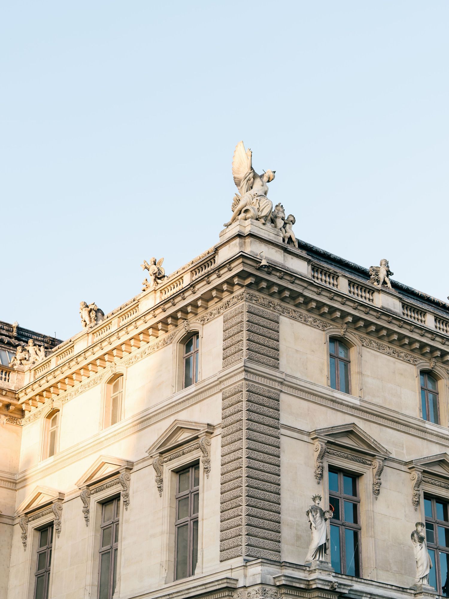 Ornate architectural details and decorative sculptures adorn the upper facade of a historic stone building in warm sunlight.