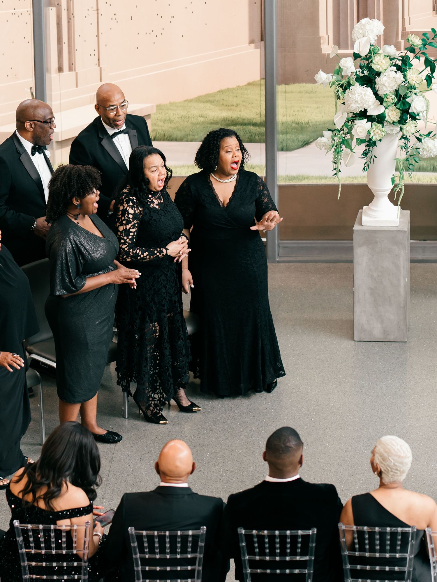 Singers perform during a formal event in an elegant venue with white floral arrangements and Chiavari chairs.