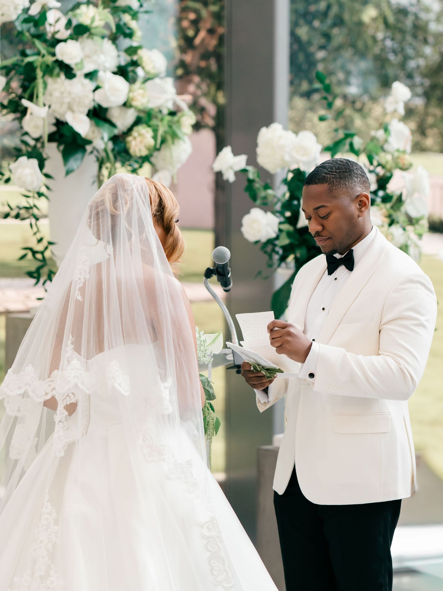 Couple exchanging vows at elegant wedding ceremony with white floral arrangements and decor at outdoor venue.