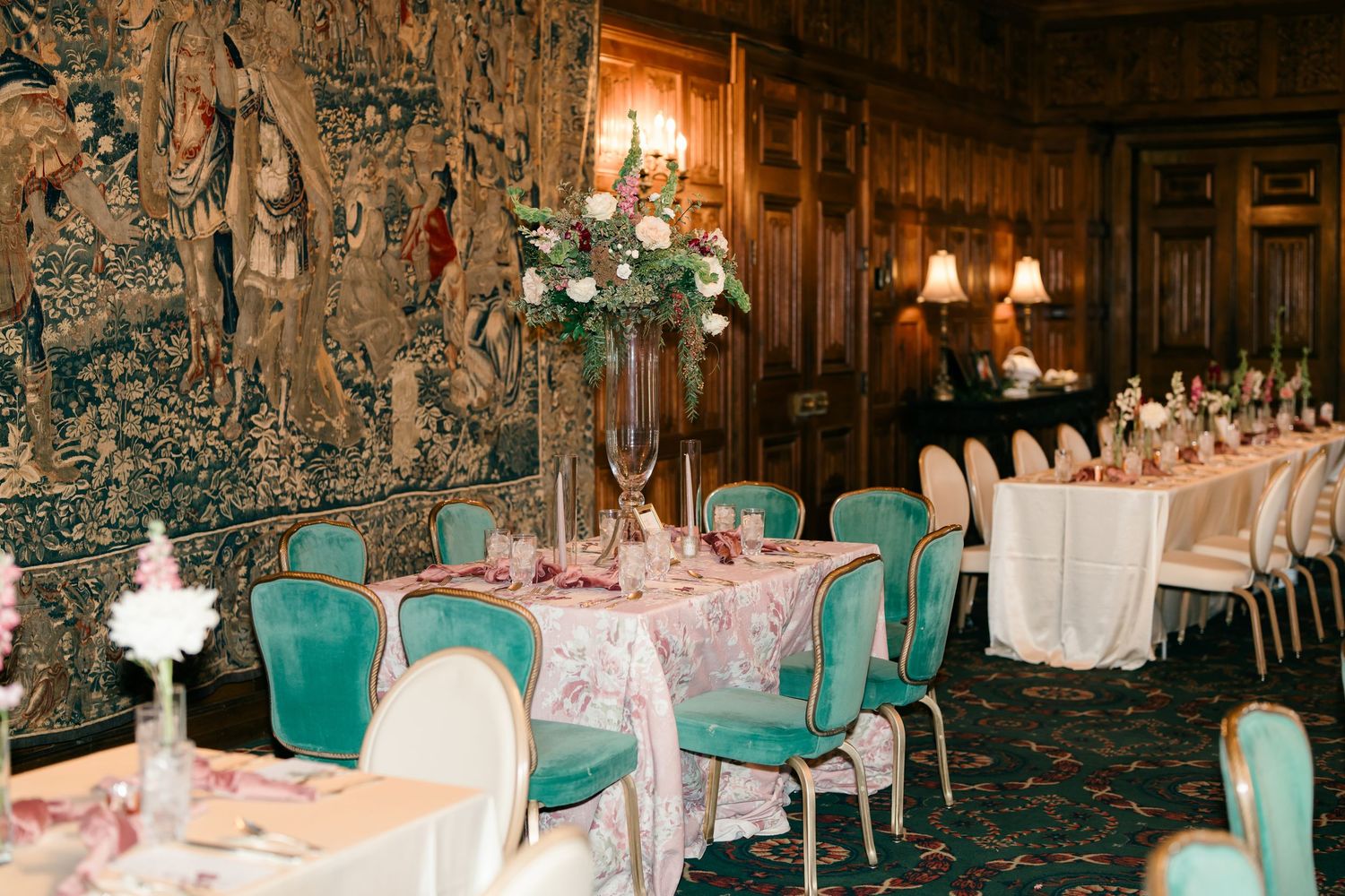 Elegant reception hall with turquoise chairs, ornate tapestries, and tall floral centerpieces set for a formal dinner event.