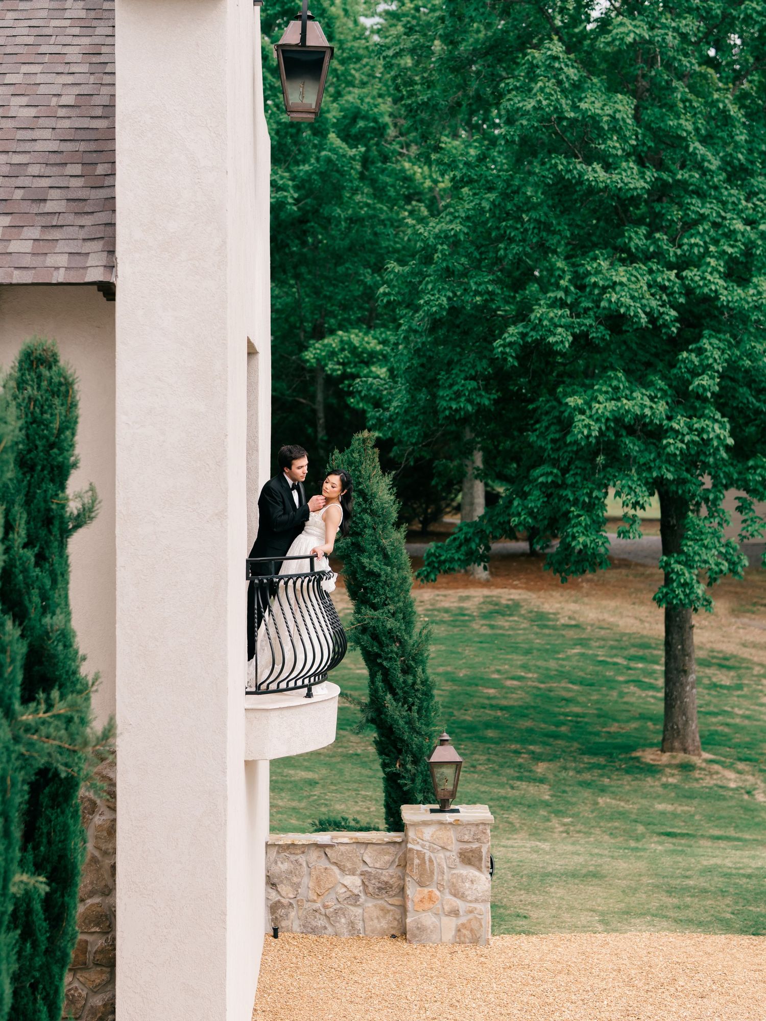 Couple sharing a romantic moment on an elegant balcony surrounded by lush green trees at a wedding venue.