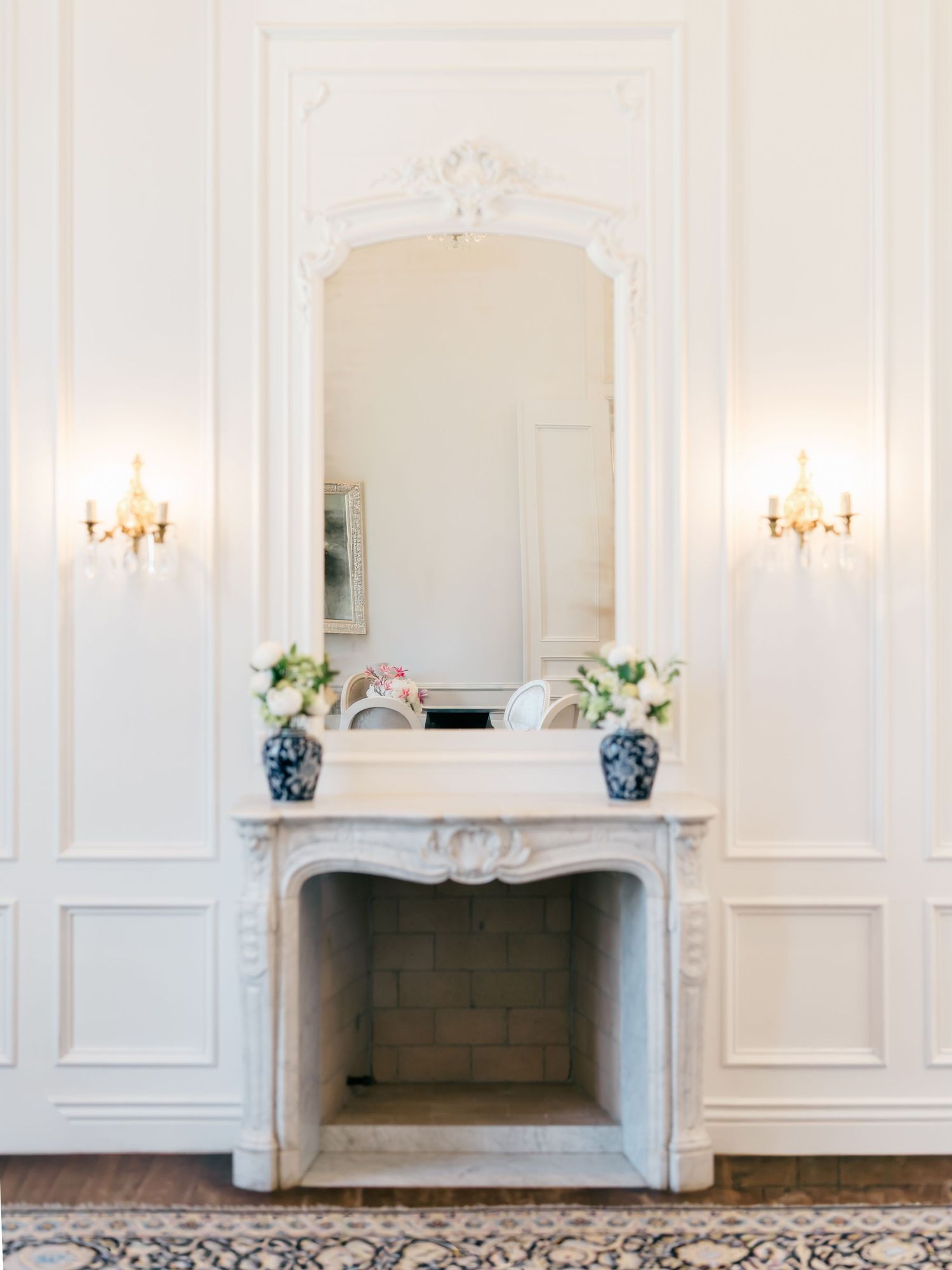 Classic white room with ornate wall moldings, fireplaces, and crystal sconces creating an elegant reception space.