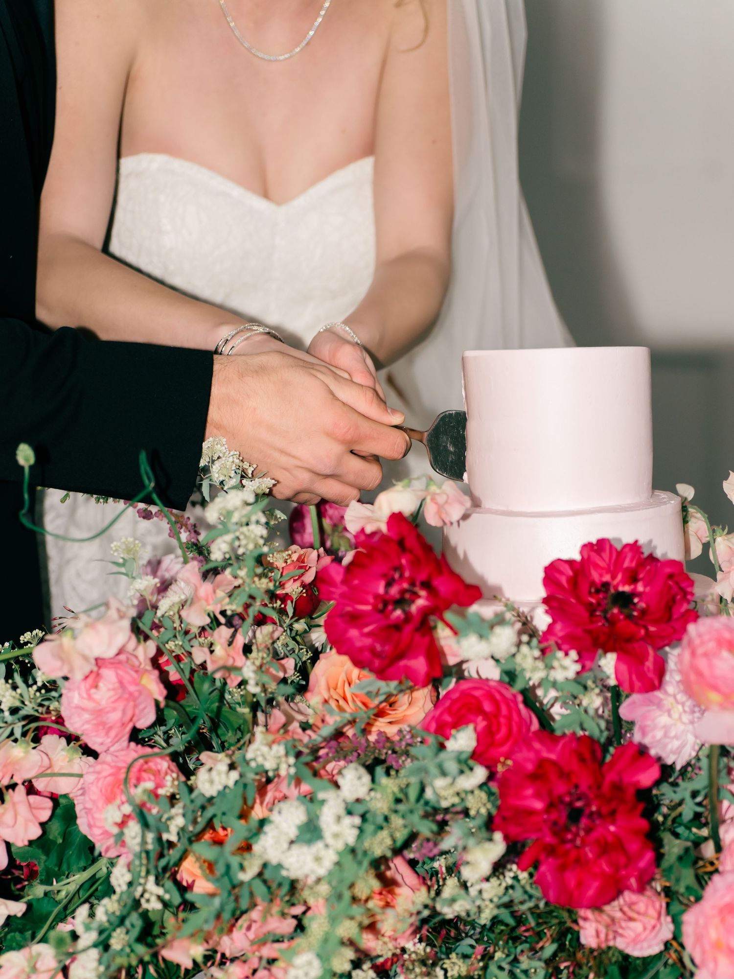 White wedding cake displayed among lush pink and red floral arrangements on an elegant table setting.