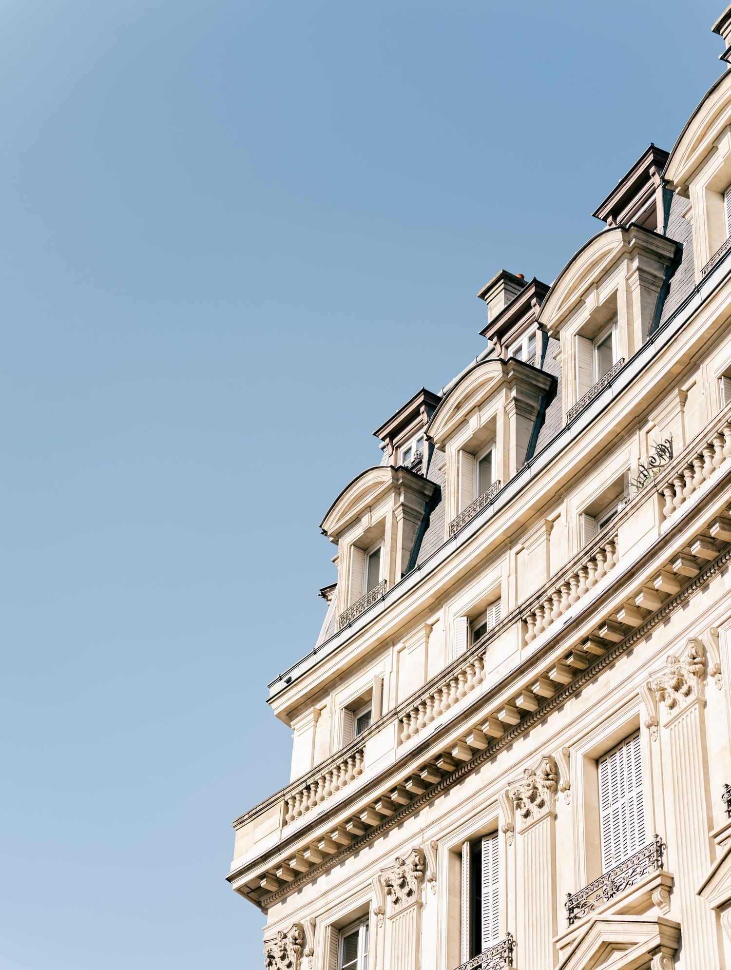 Classic Parisian apartment building with ornate white stone facade and traditional mansard roof against blue sky. Paris, France.