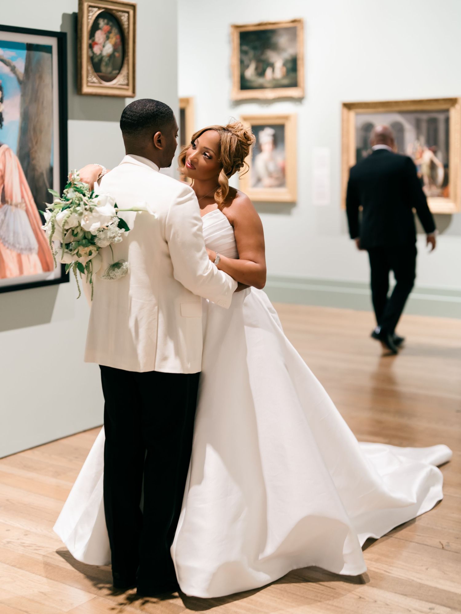 A romantic couple shares an intimate moment in a museum gallery surrounded by artwork on white walls.
