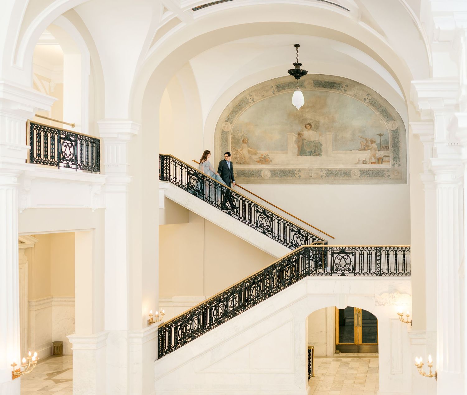 Elegant white marble staircase with ornate black iron railings in a luxurious classical interior with arched ceilings.