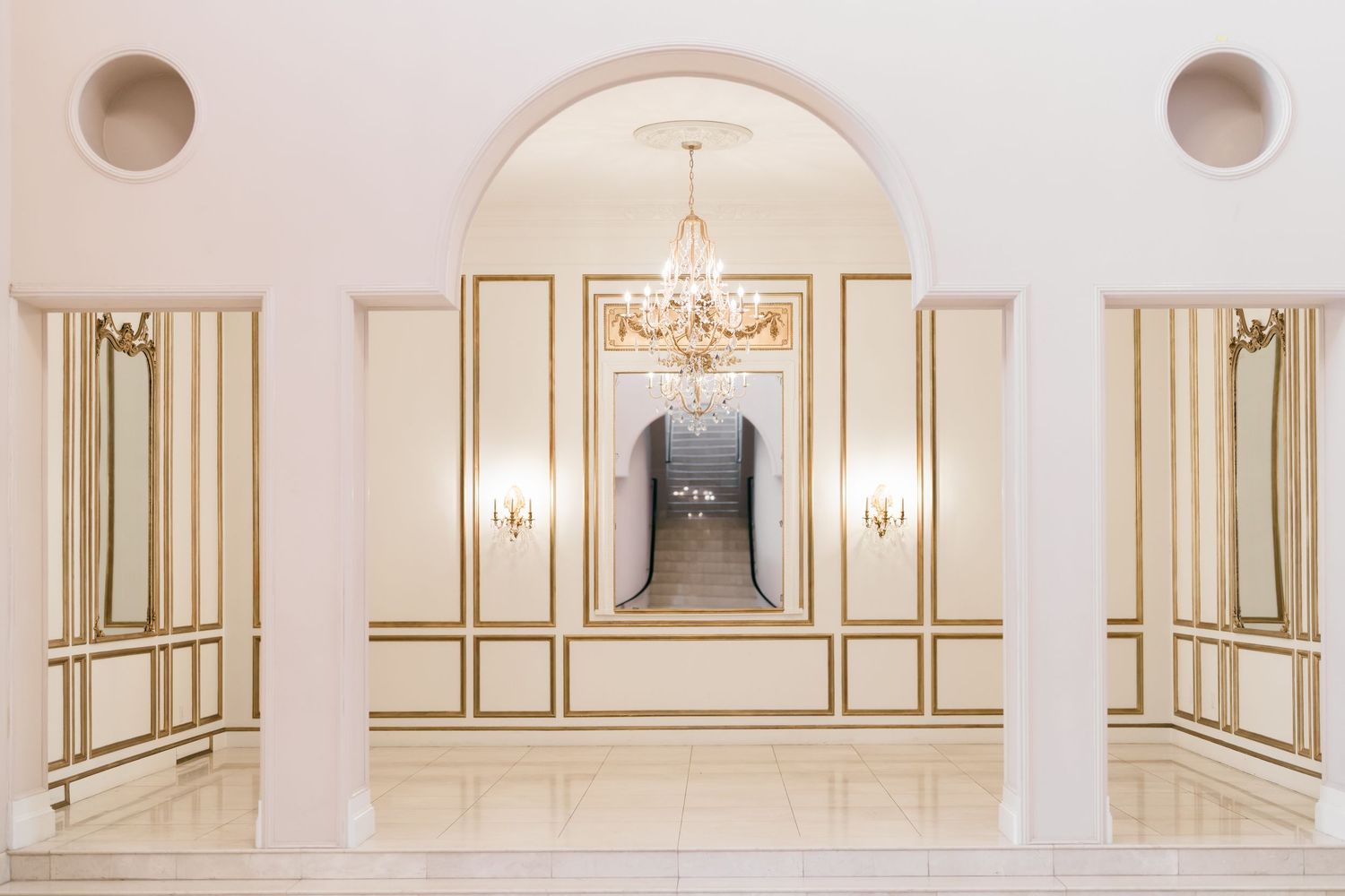 Elegant white and gold ballroom interior with ornate moldings, crystal chandeliers, and classic architectural details.