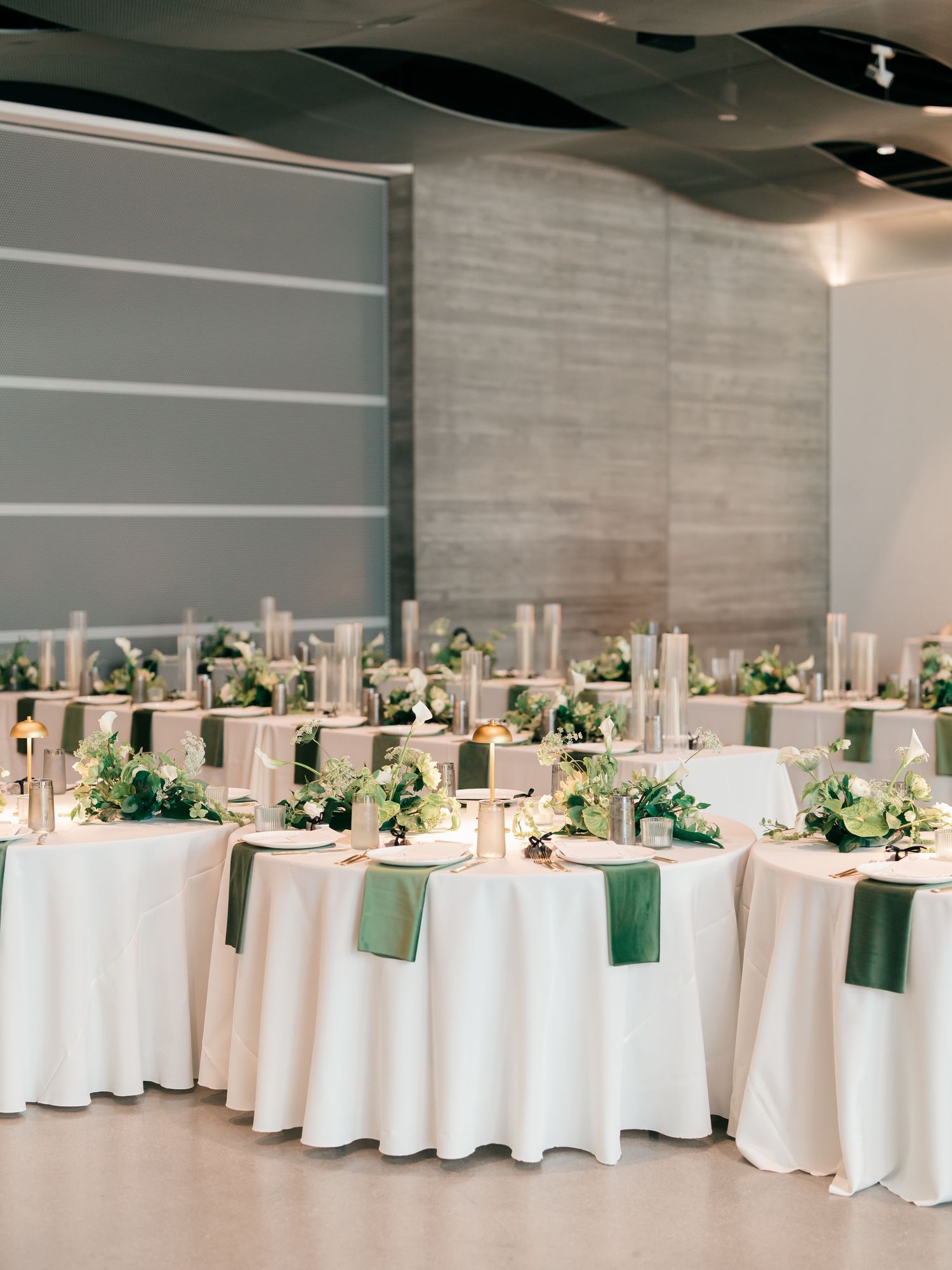 Elegant wedding reception setup with round tables draped in white linens and decorated with green floral centerpieces.