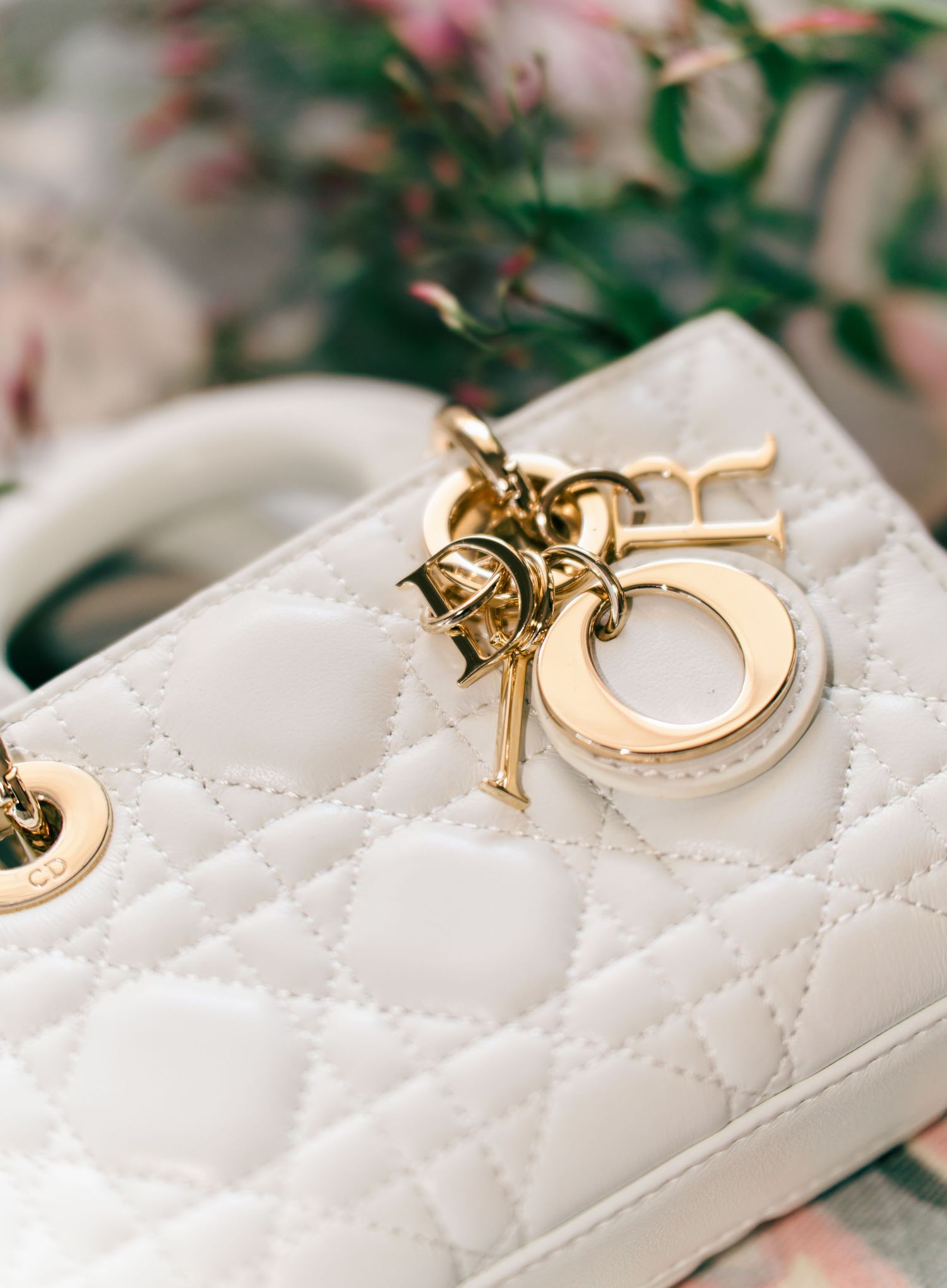 Close-up of a white quilted leather Dior handbag with gold chain and charm details.