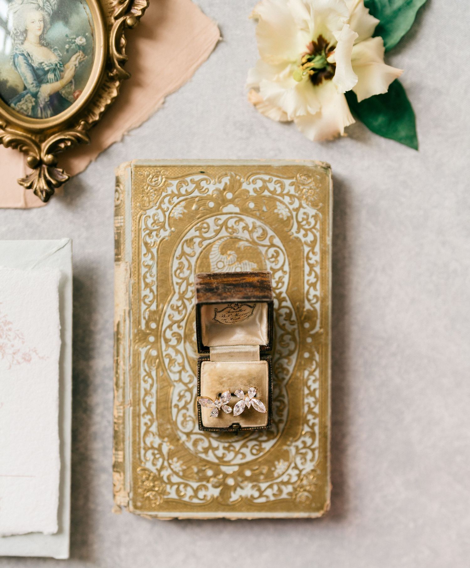 Ornate gold wedding ring boxes with delicate white floral decorations and white flowers arranged on a light surface.
