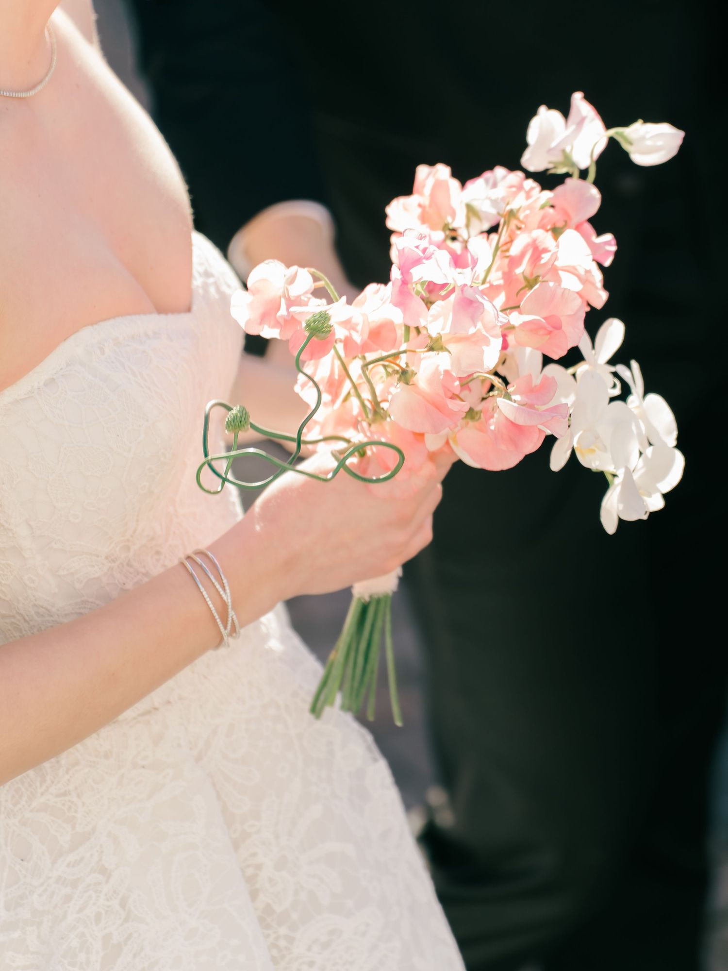 Close-up view of a bridal bouquet featuring delicate pink and white orchids against a dark background.