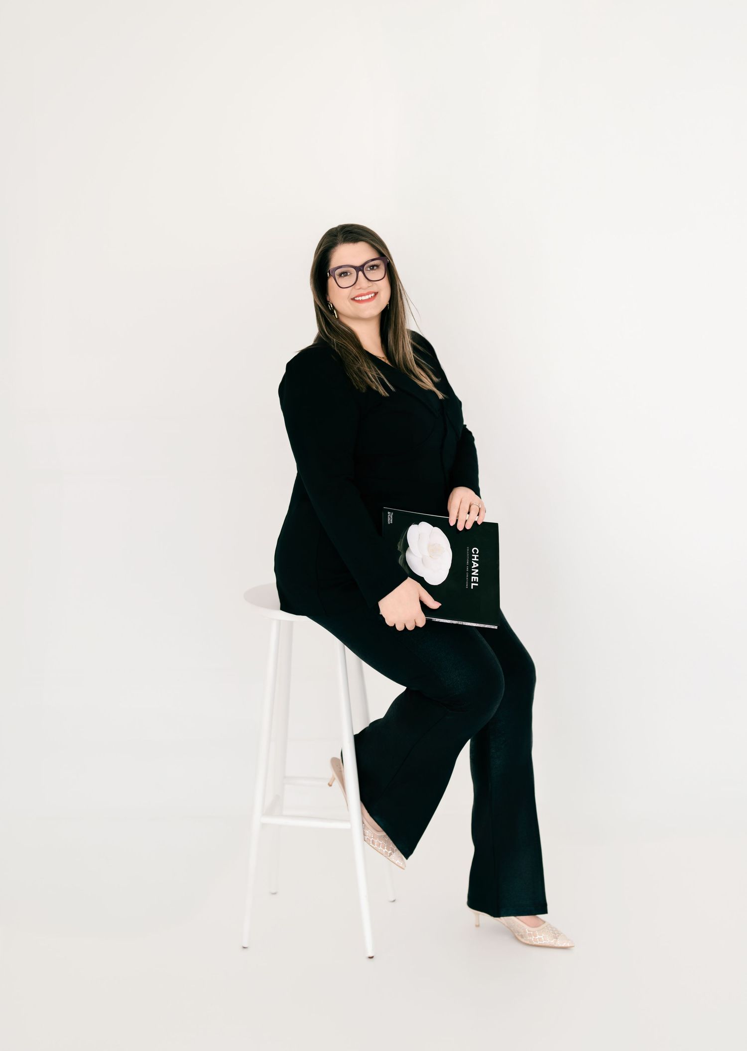 Modern business portrait sitting on white stool wearing black outfit with white accents.