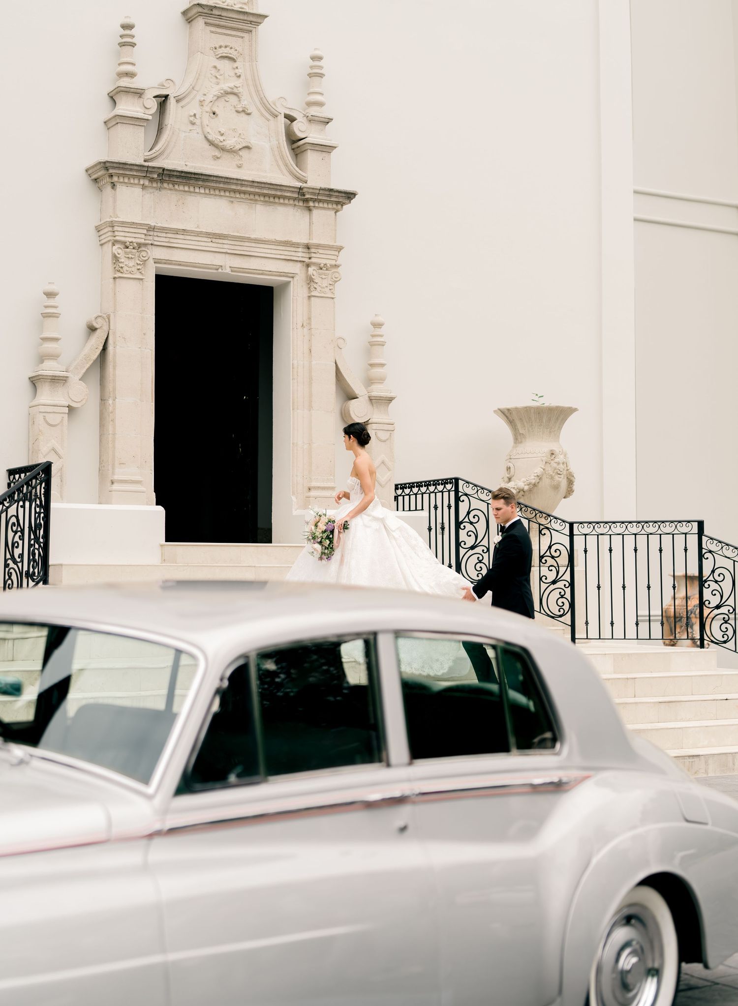 Classic white vintage Rolls Royce cars lined up outside an elegant white stone church entrance.