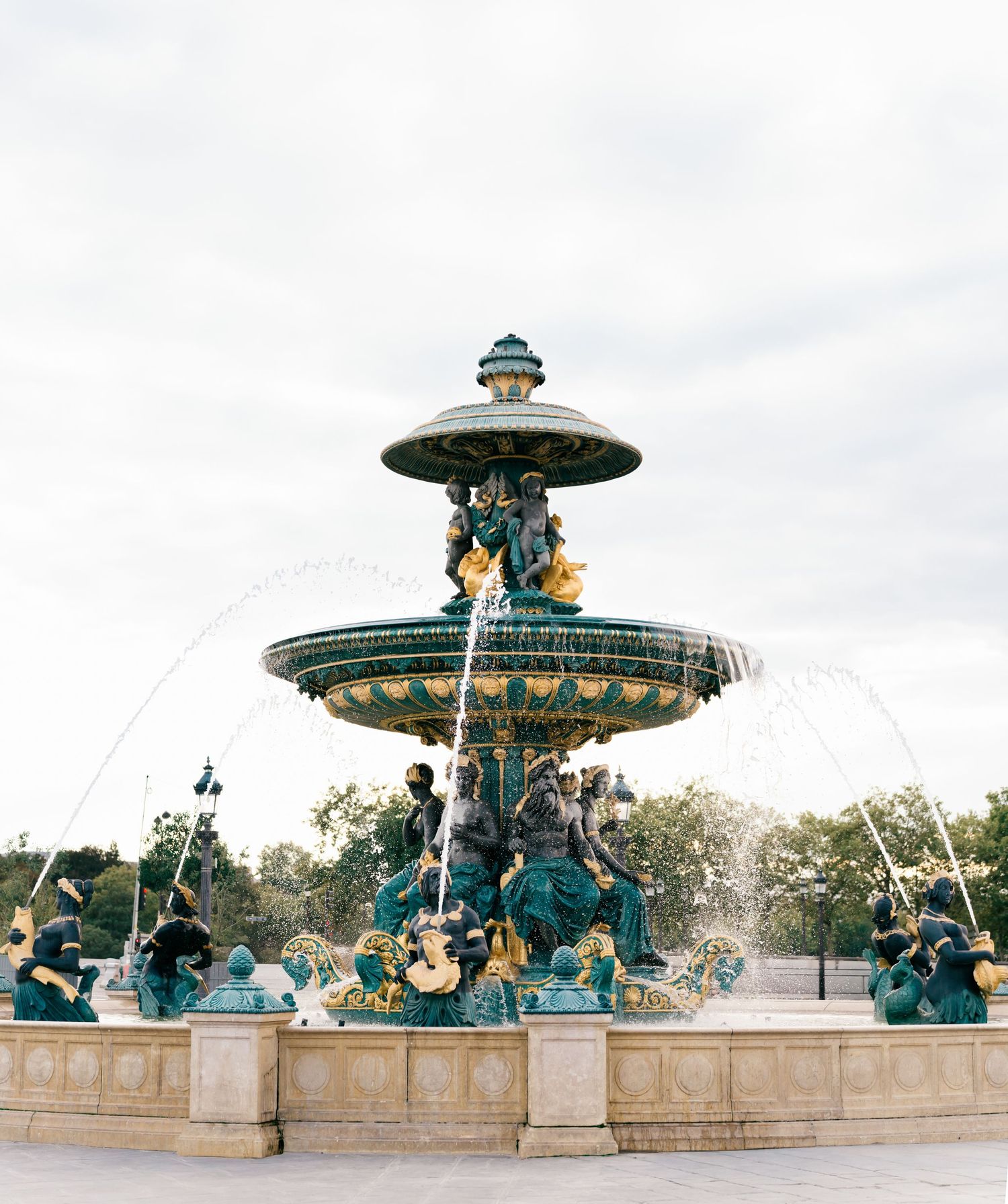 Ornate green and gold fountain with multiple tiers and cherub statues stands majestically in Place de la Concorde, Paris, France.
