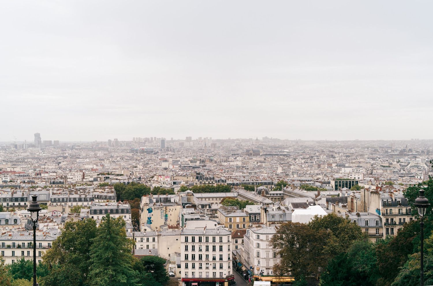 Aerial view of Paris cityscape with historic buildings and rooftops stretching to the horizon on a cloudy day.