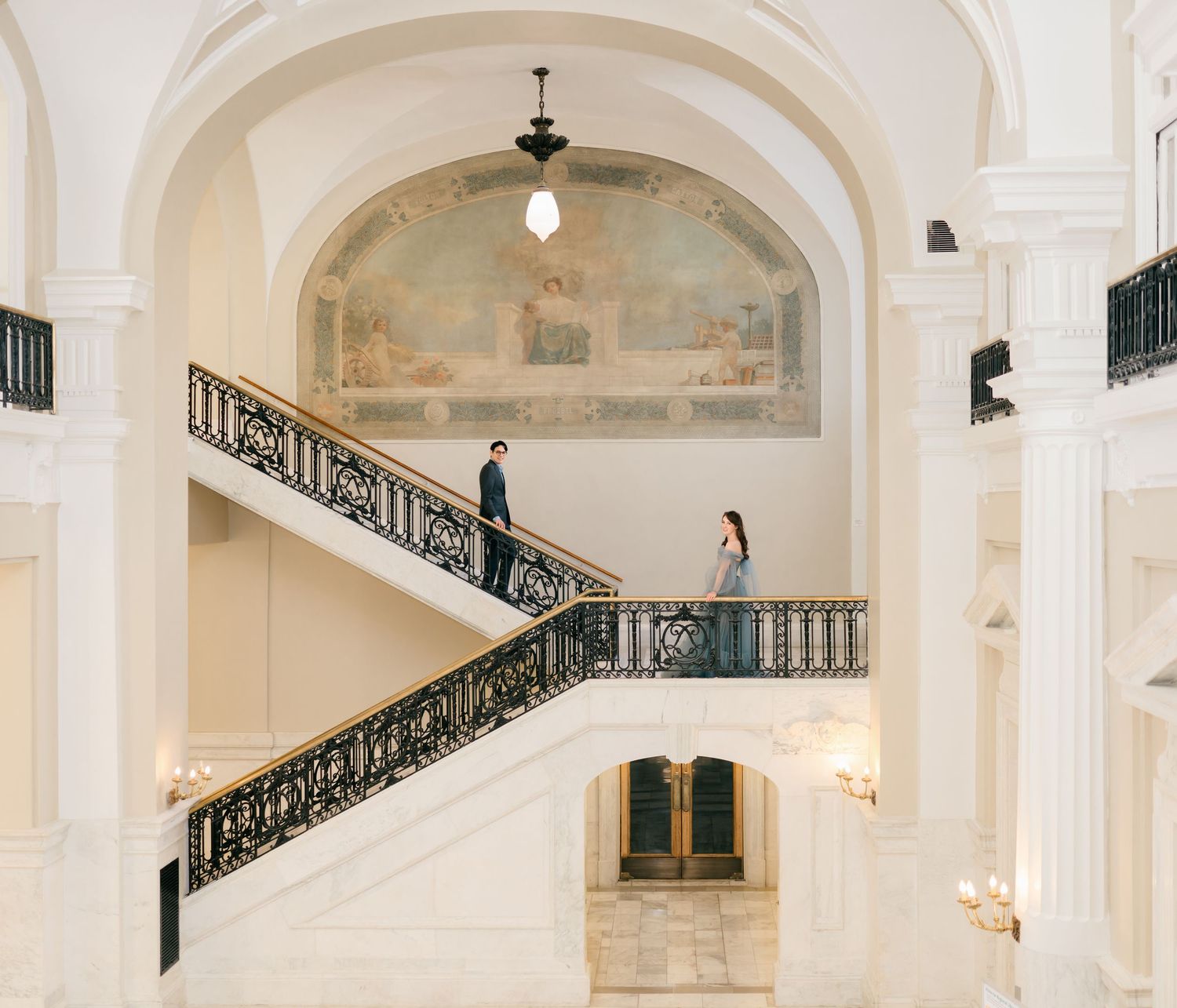 Elegant white marble staircase with ornate black iron railings in a grand historic building interior.