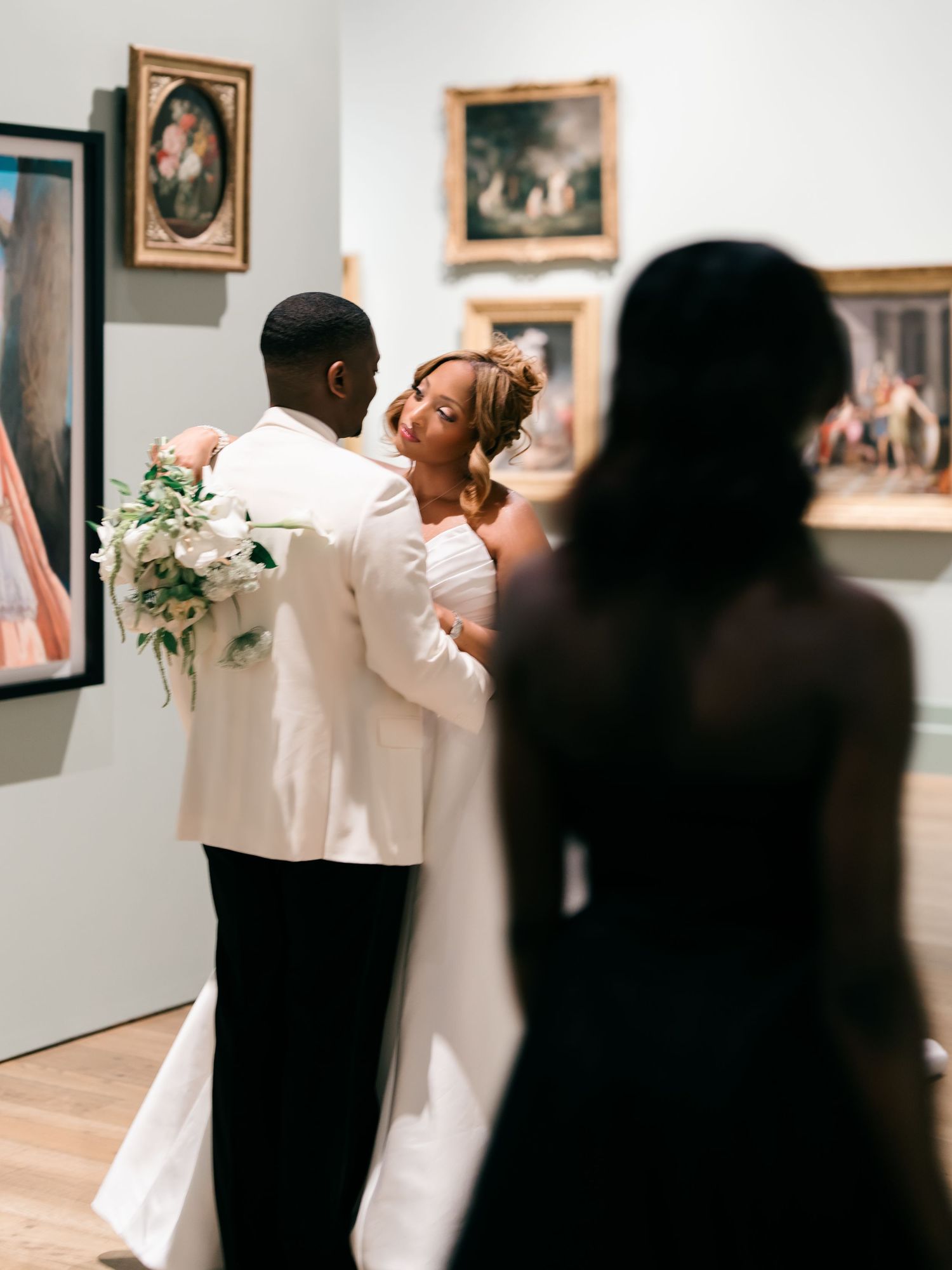 A couple shares their first dance at a museum wedding surrounded by framed artwork on gallery walls.