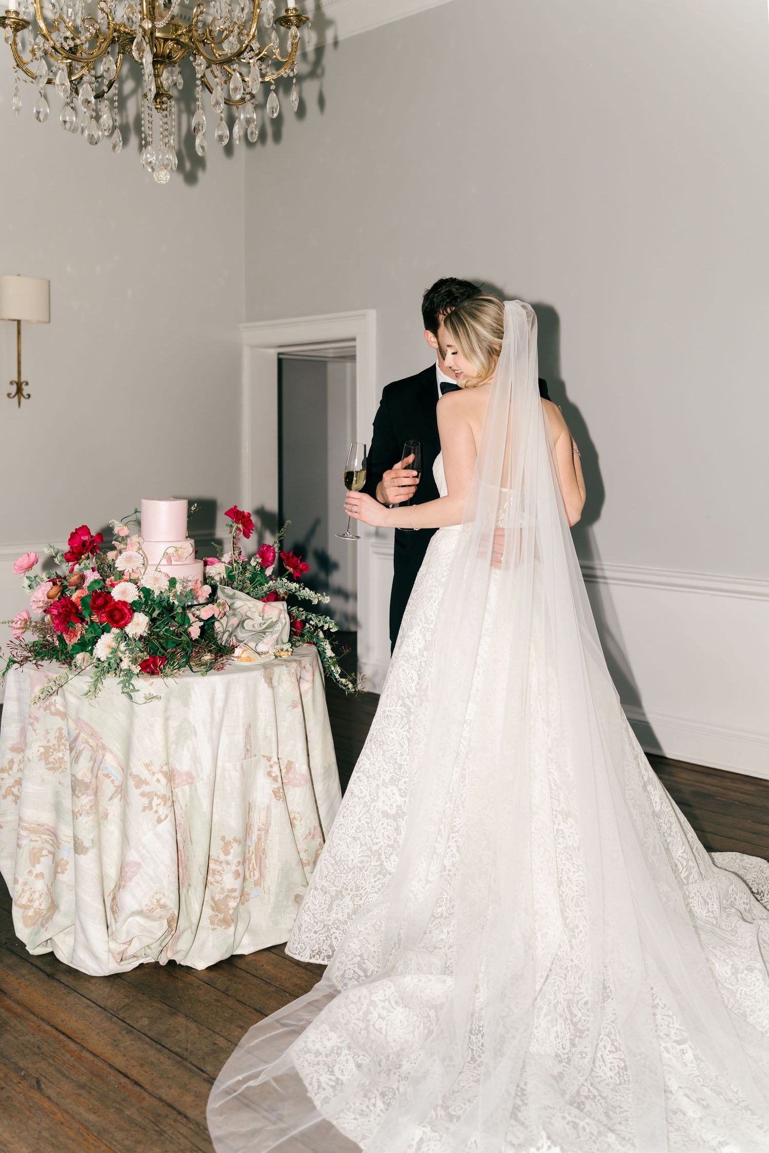 A series of four elegant white wedding gowns with lace details displayed in a room with crystal chandeliers.