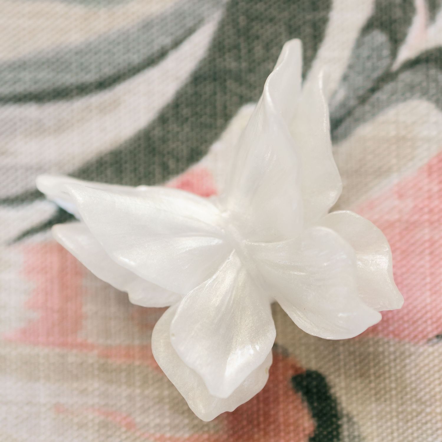 Delicate white mother of pearl butterfly decoration on a floral patterned fabric background.