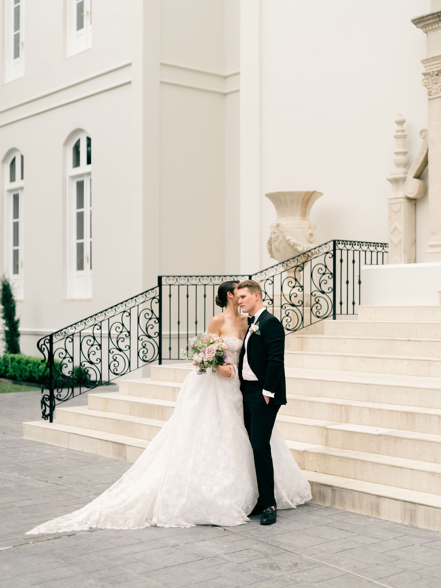 Couple in formal attire sitting on grand white stone steps of an elegant building.