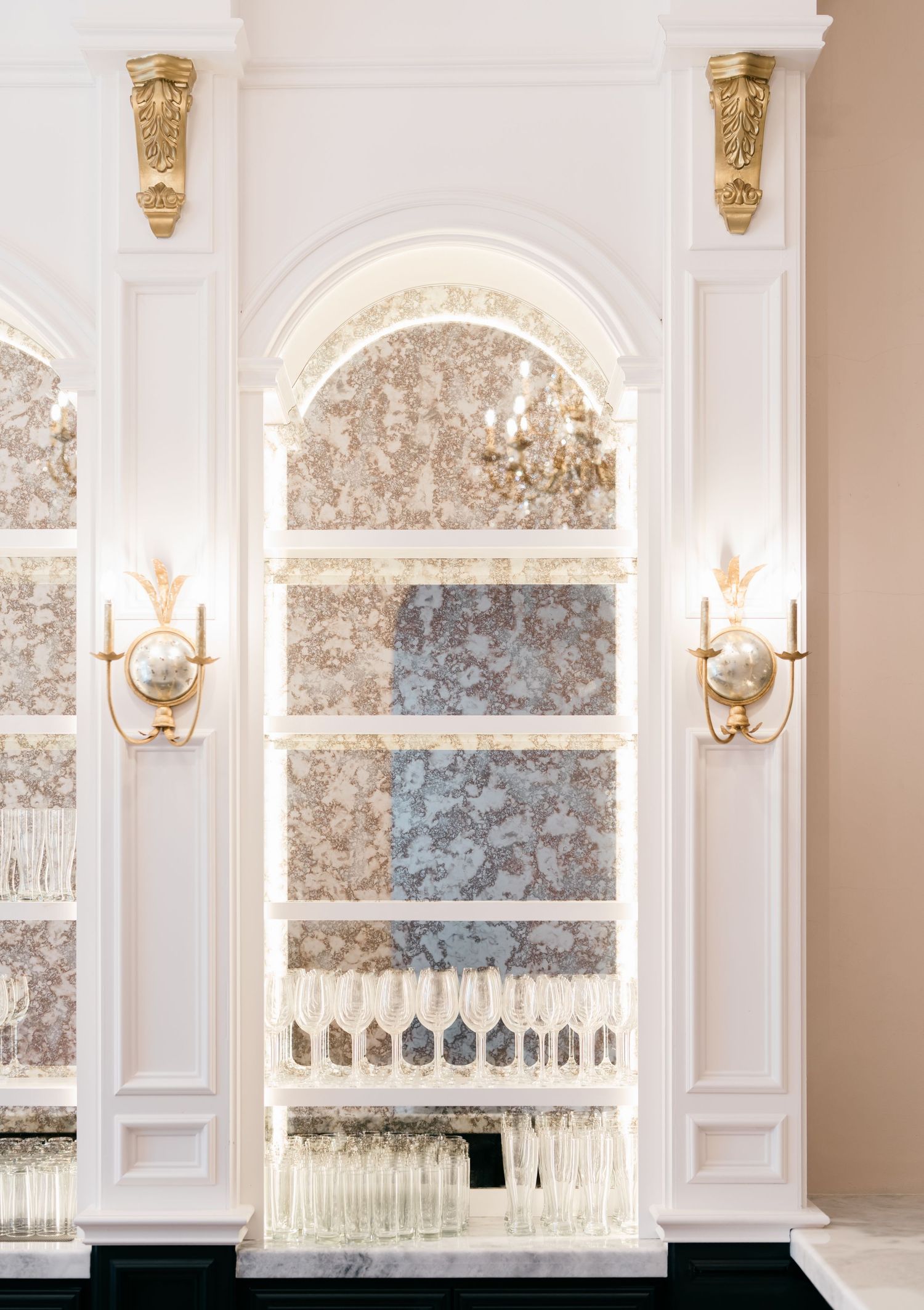 Elegant white paneled wall with crystal sconces and decorative arched window featuring delicate floral wallpaper accents.