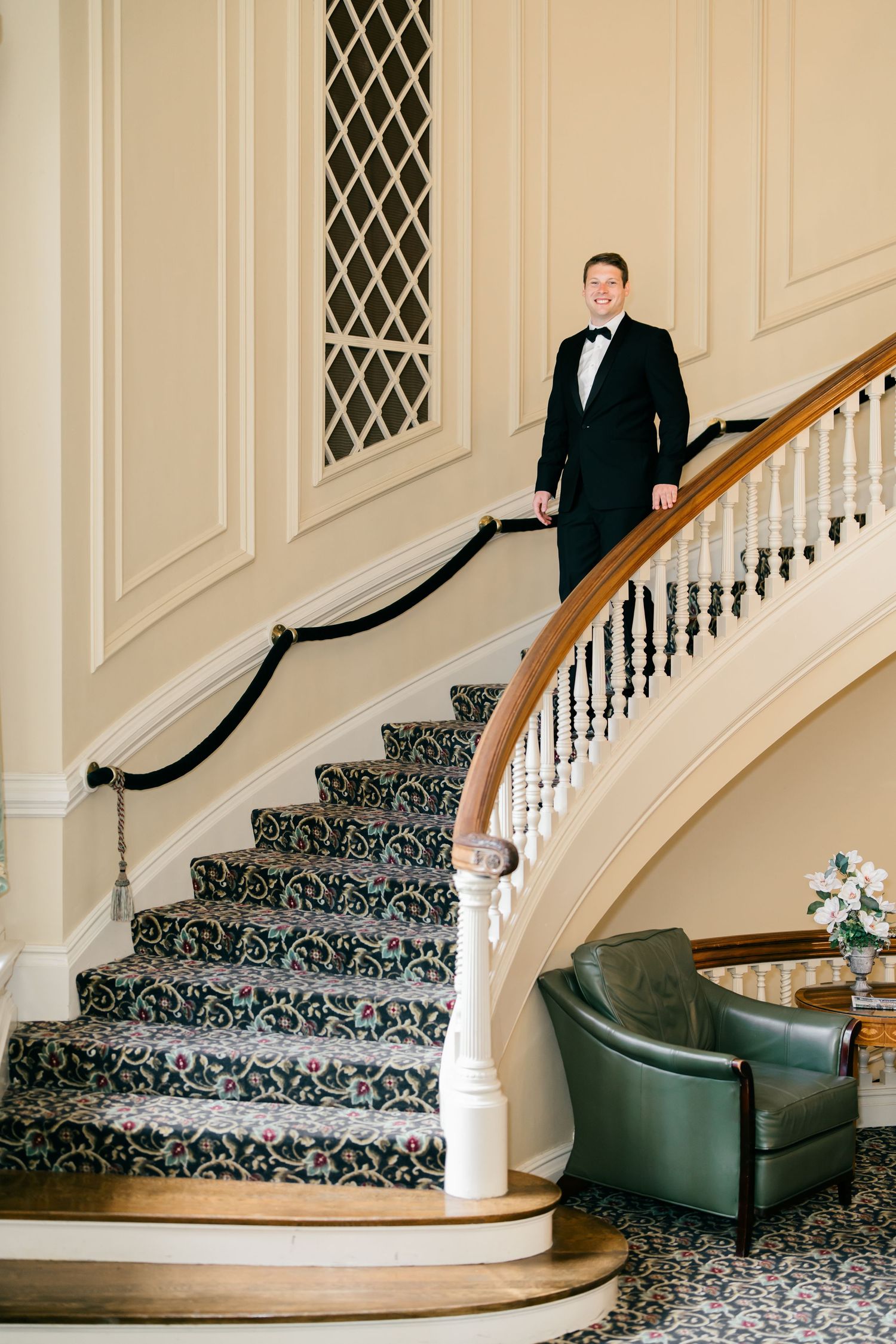 Elegant curved staircase with ornate patterned carpet runner and dark wood handrail in a classic cream-colored interior.