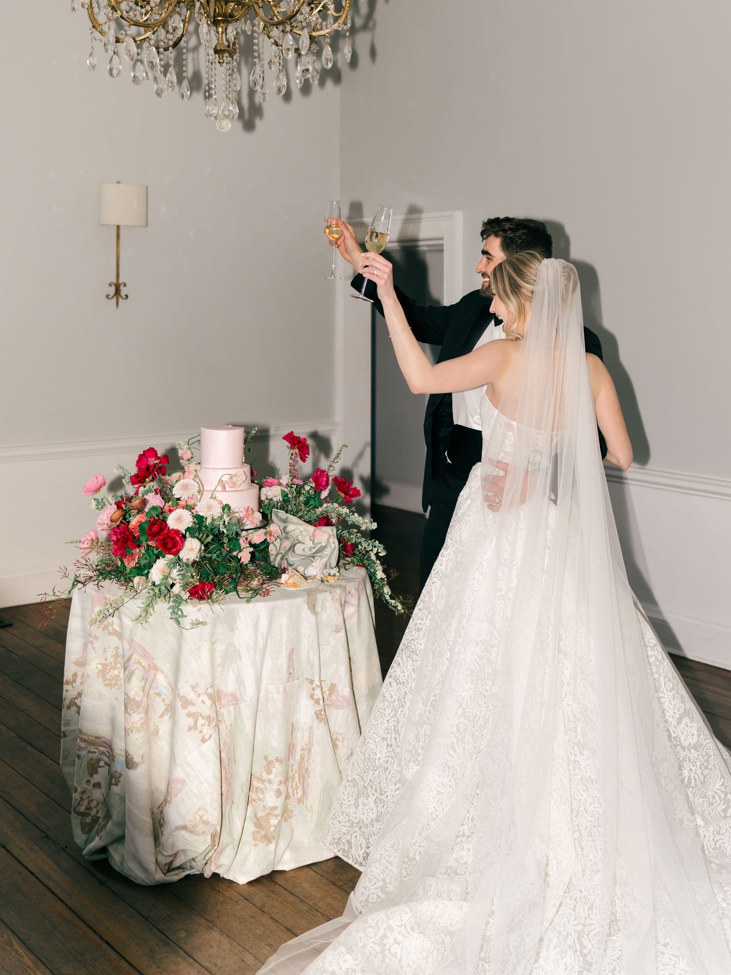 Elegant wedding reception setup with crystal chandelier and floral arrangements in a light-filled room.