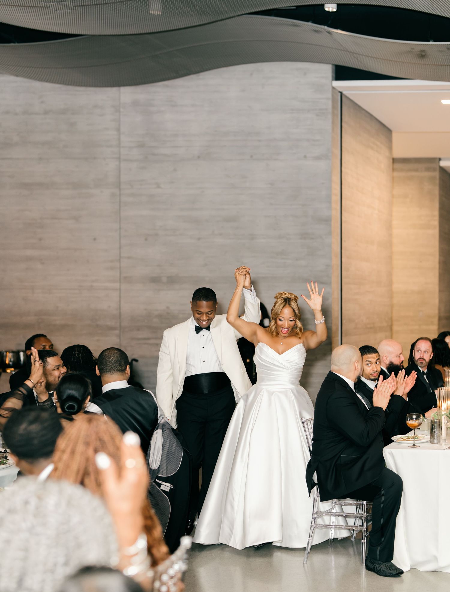 Wedding guests celebrating and raising their hands in joy during a wedding reception in a modern indoor venue.