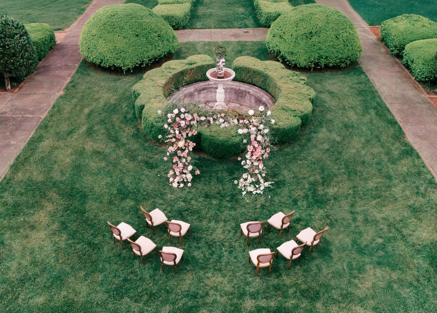 Aerial view of a garden maze with manicured hedges and decorative white furniture arranged in a circular pattern.
