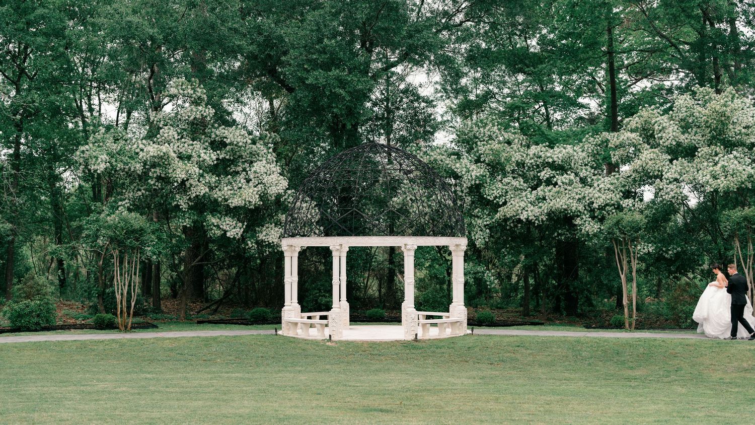 A scenic garden venue with stone archways and green landscaping creates an elegant outdoor setting.