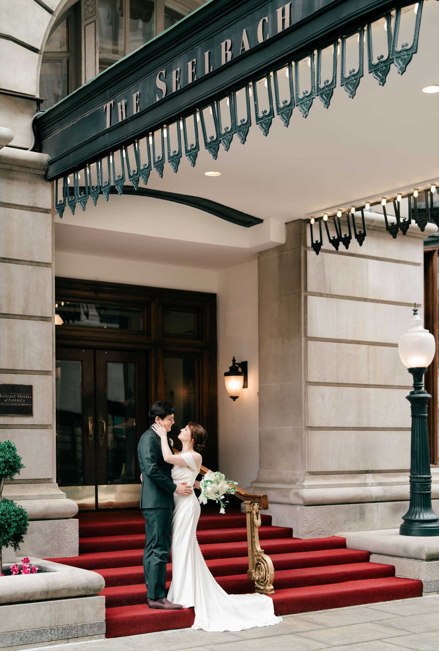 A couple poses on red-carpeted steps outside The Seelbach luxury hotel entrance with elegant architectural details.