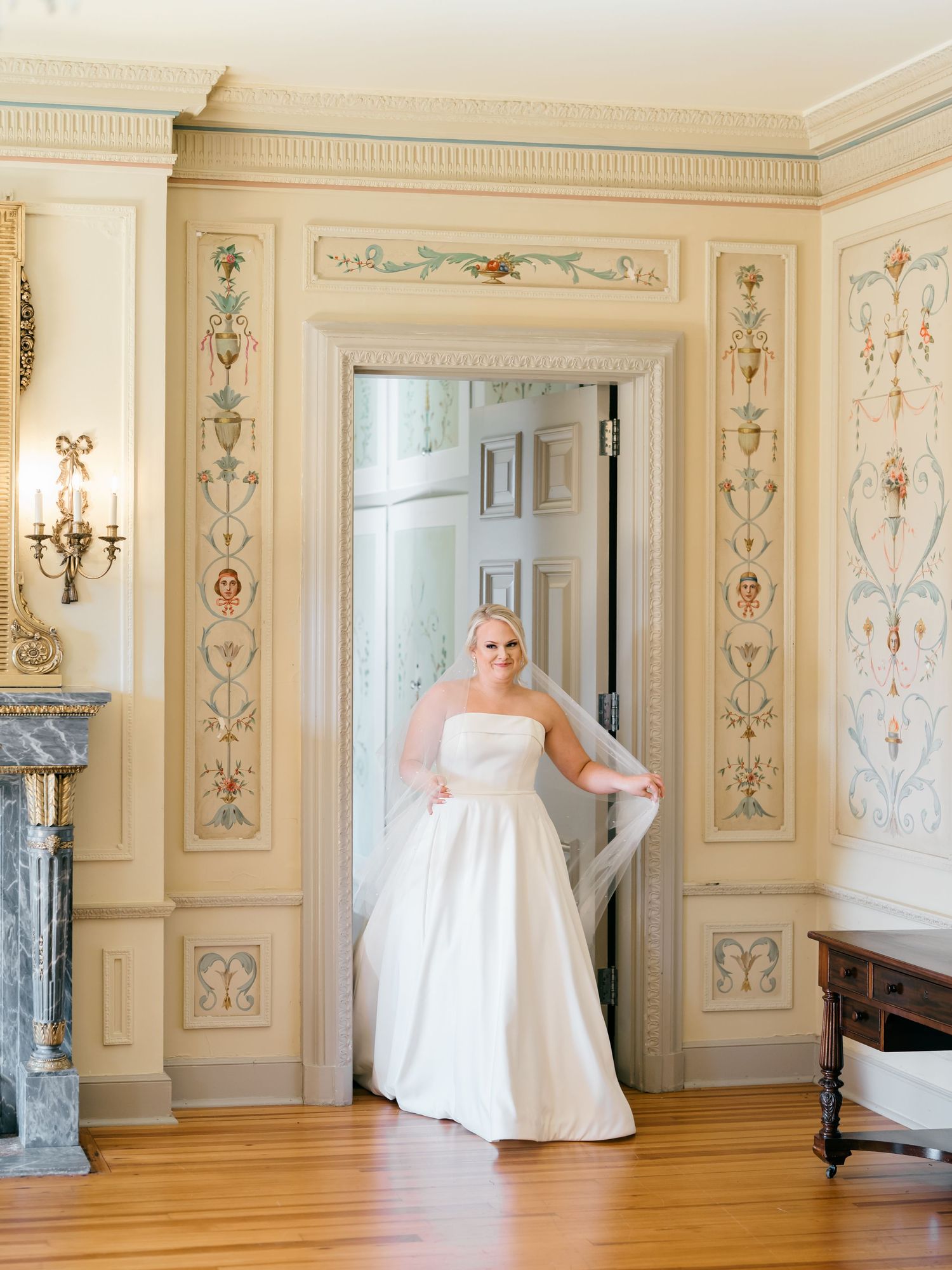 Elegant ballgown in a classical room with ornate wall panels and decorative moldings.