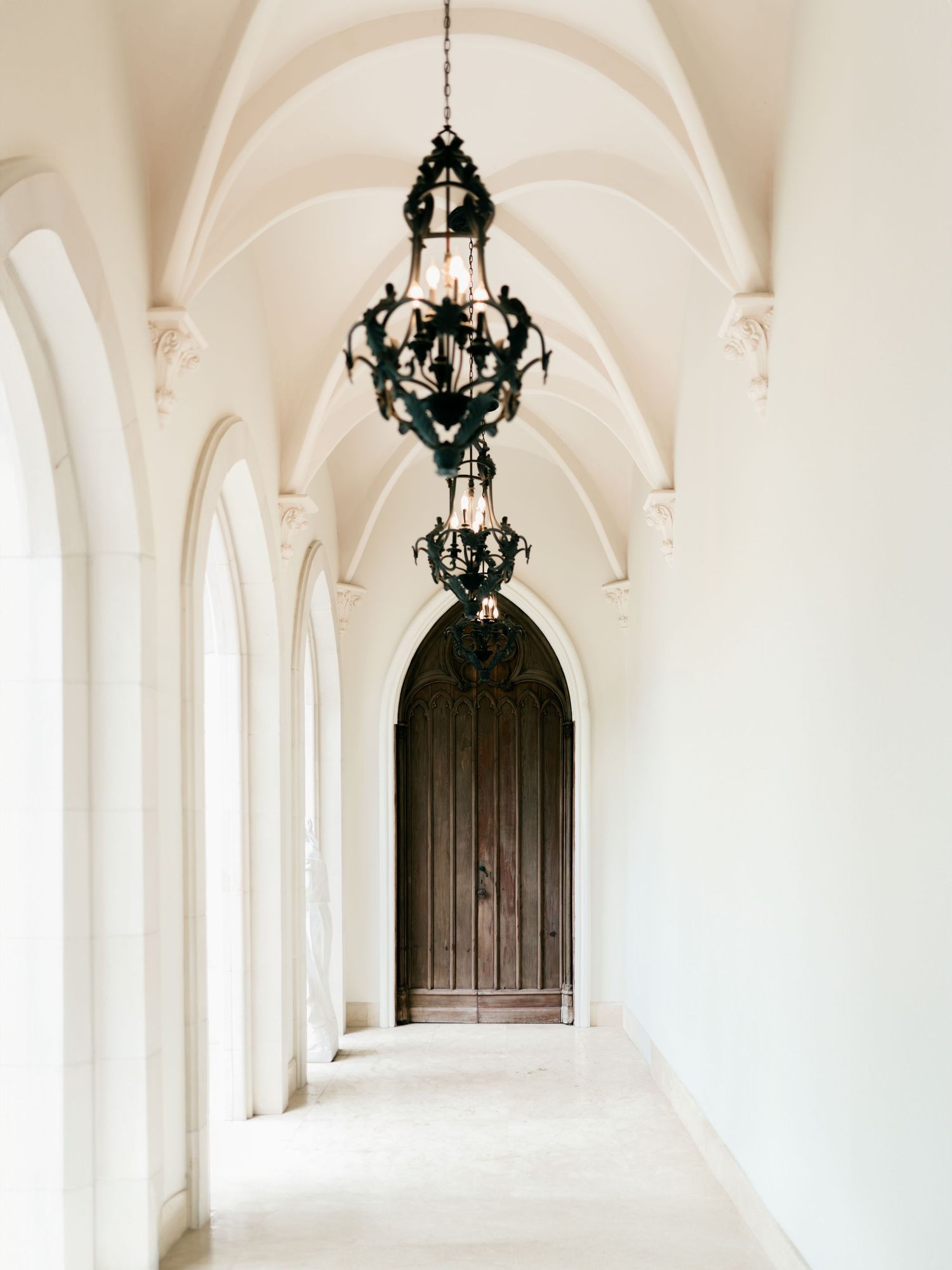 Elegant white arched hallway with ornate black chandeliers creating a dramatic contrast against the bright interior.