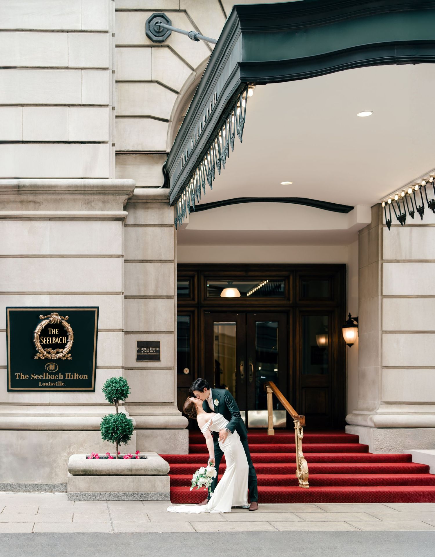 A couple sharing a romantic moment outside the grand entrance of the Ritz Hotel with its iconic red carpet and stone facade.