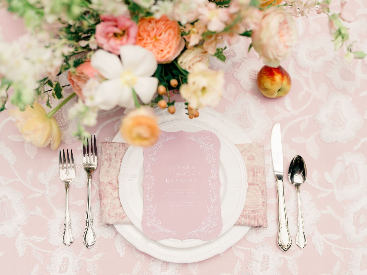 Elegant wedding table setting with soft pink and white floral arrangements, crystal glassware, and delicate place settings.