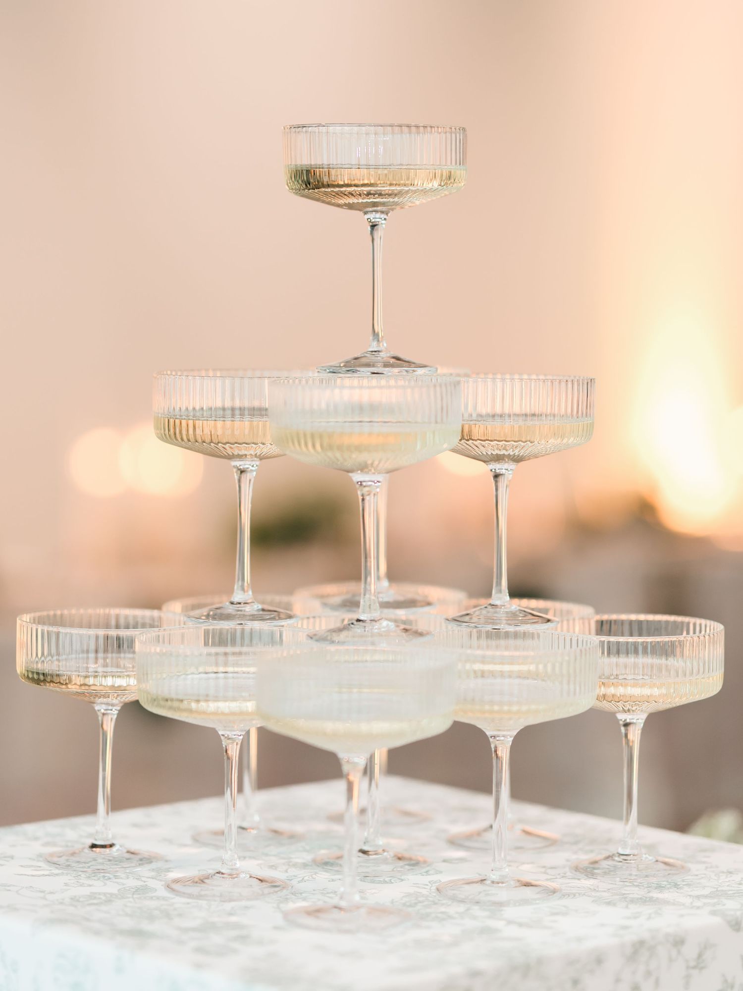 Elegant champagne tower setup with vintage-style coupe glasses arranged in tiers on a white textured surface.