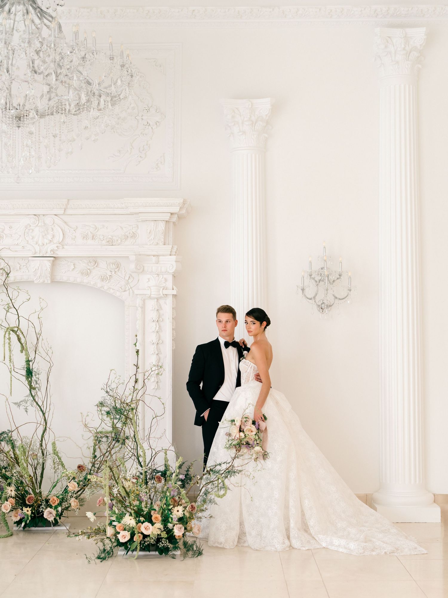 Classic white wedding venue interior with ornate columns and floral arrangements. A bride and groom portrait at Chateau, Nouvelle. Texas.