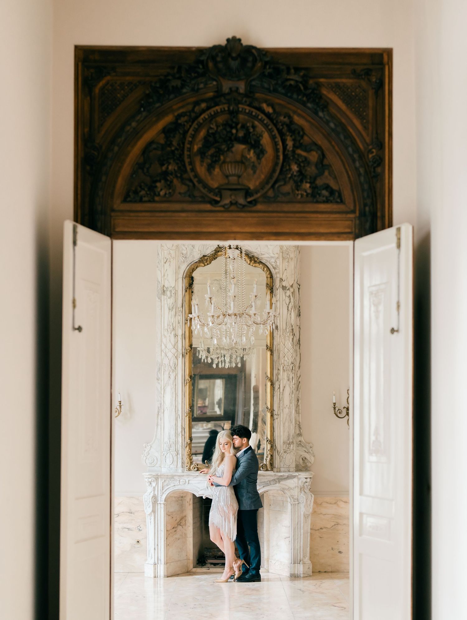 Couple dancing in an elegant white ballroom with ornate architectural details and crystal chandeliers.