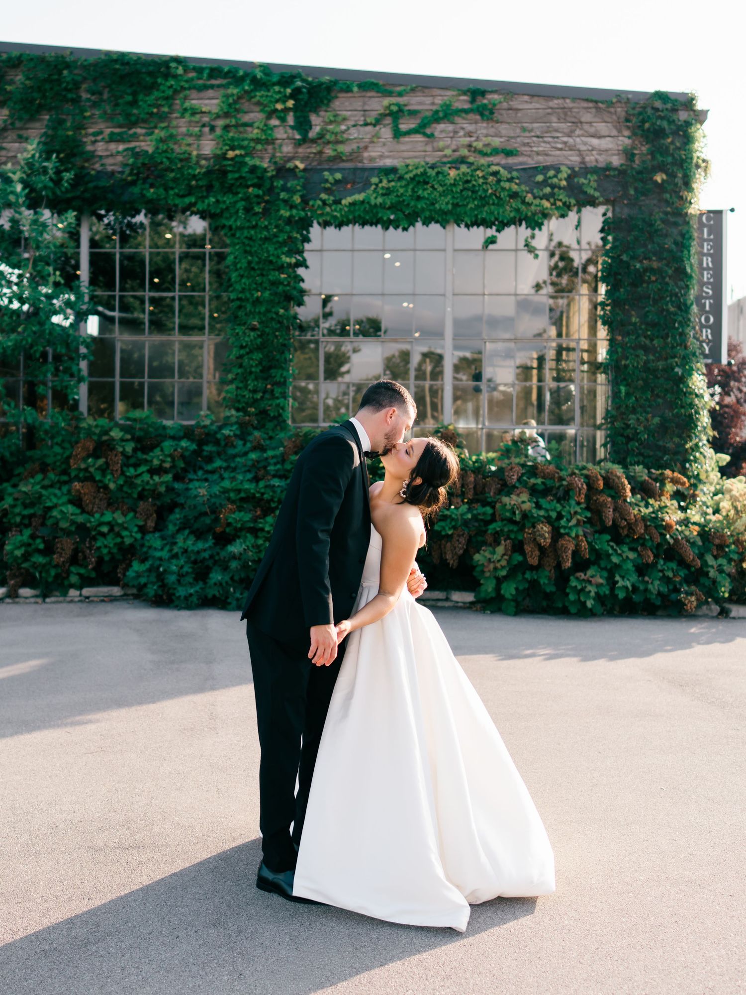 Bride and groom share a romantic kiss outside an ivy-covered wedding venue on their special day.