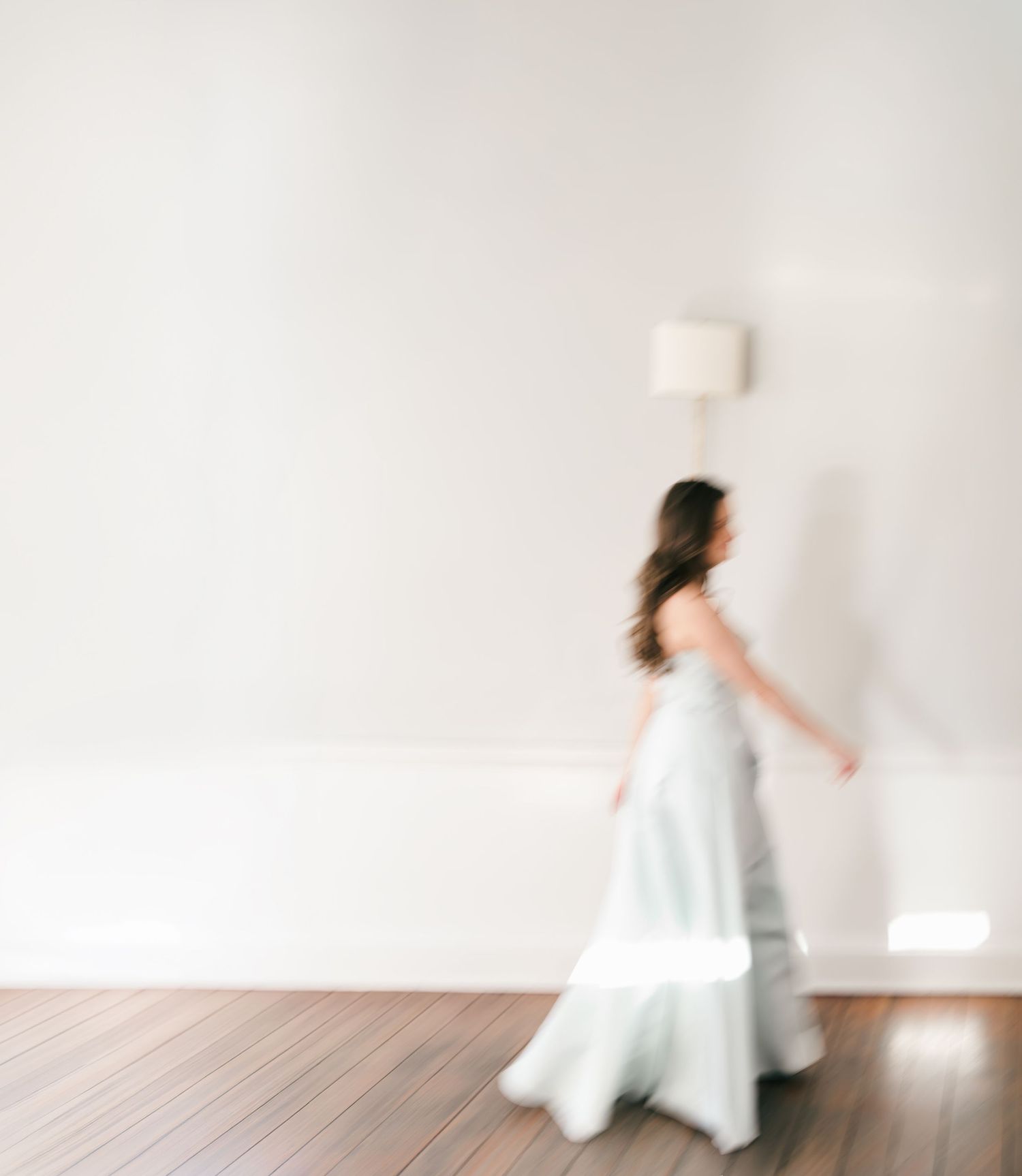 Artistic motion blur photograph of a flowing white dress against a minimalist white background.