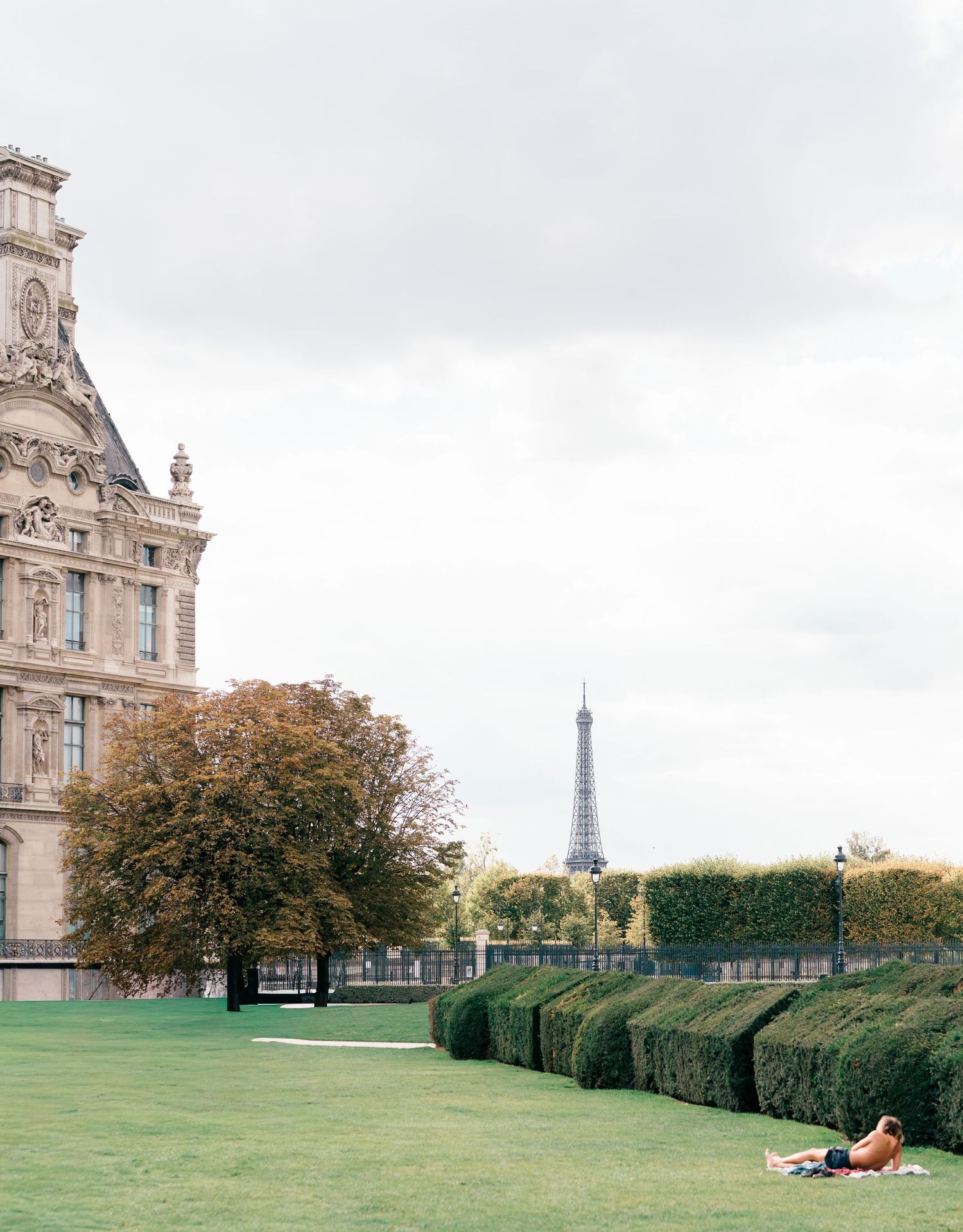 View of the Eiffel Tower in the distance across a manicured lawn with trimmed hedges in the Tuileries Garden of Paris.