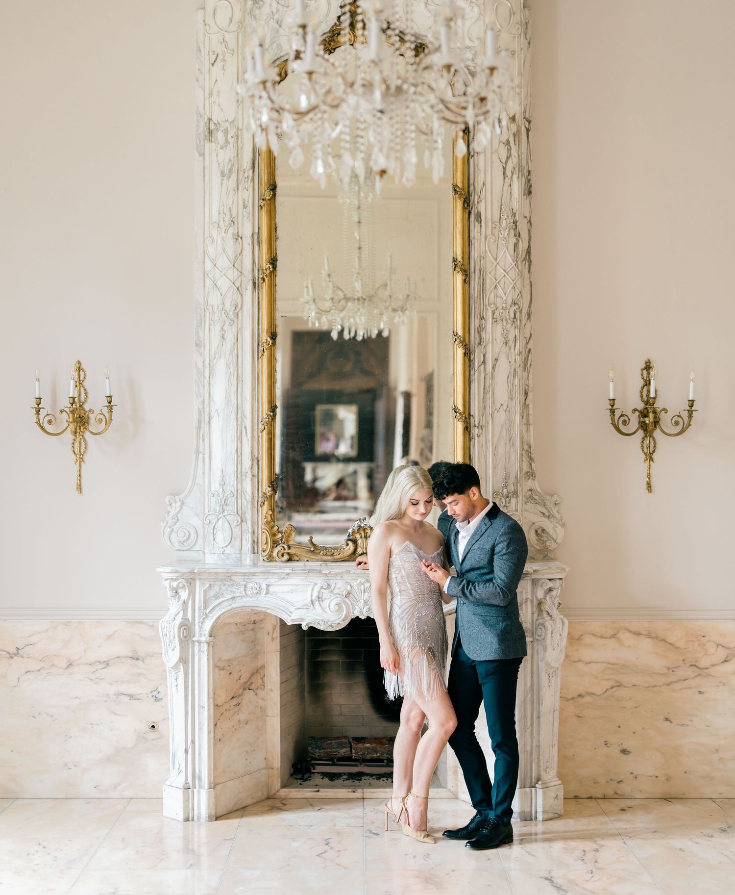 A romantic couple shares an intimate dance in an elegant marble room with ornate wall sconces and crystal chandeliers.