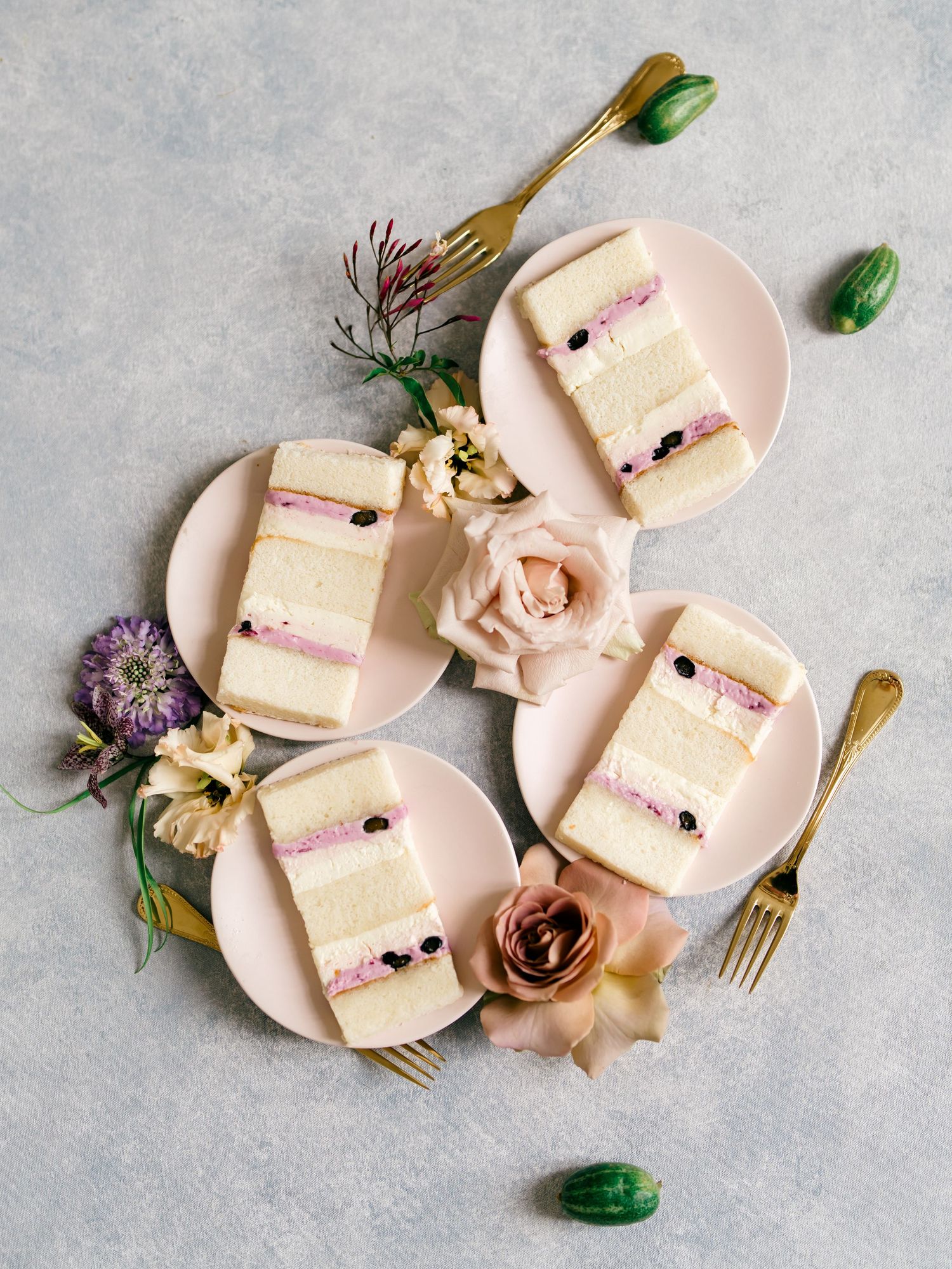 Slices of vanilla cake with pink frosting arranged on blush plates with floral decorations and gold utensils.