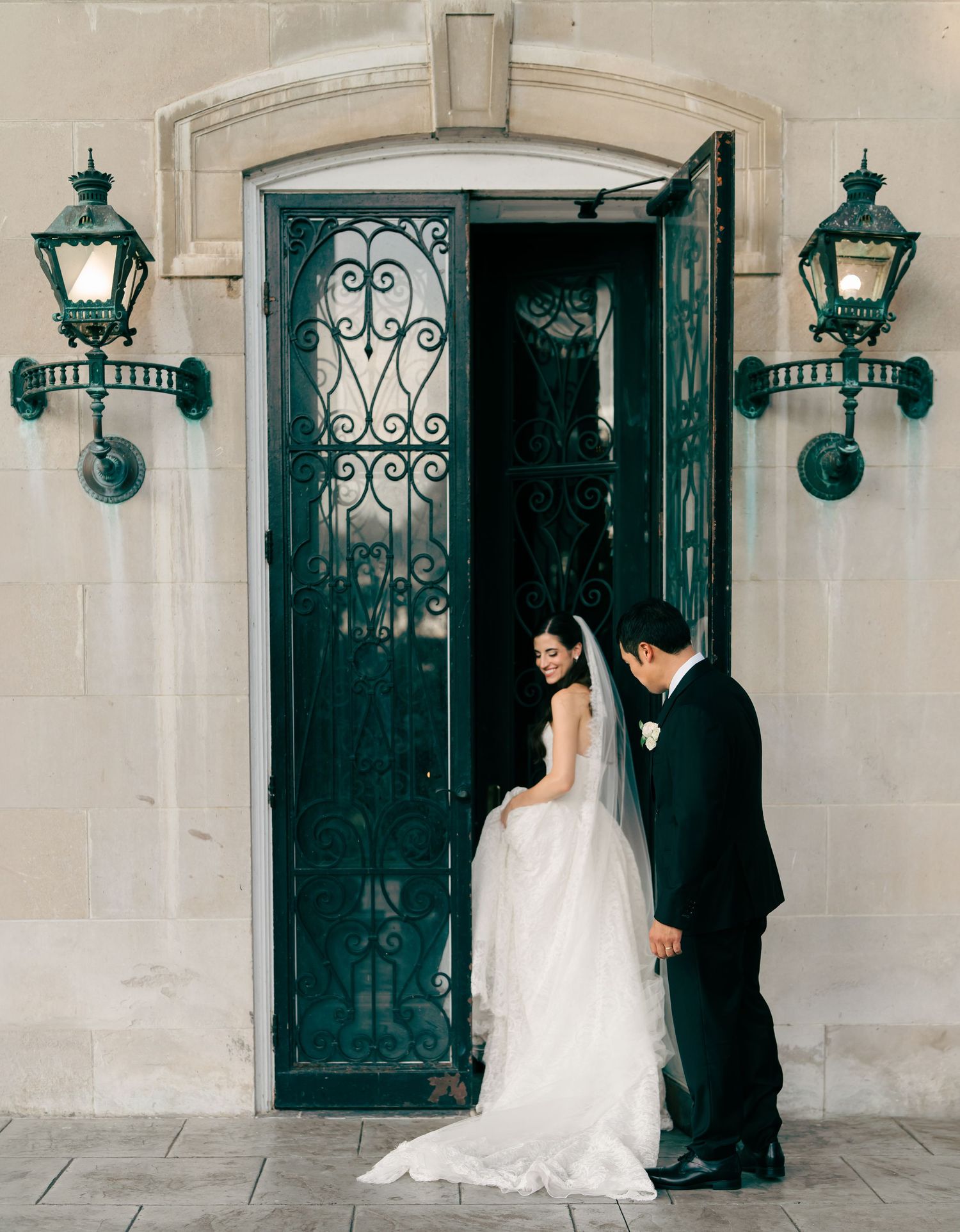 Bride and groom share a romantic moment at ornate green iron doors flanked by vintage lanterns at Spindletop Hall in Lexington, Kentucky.