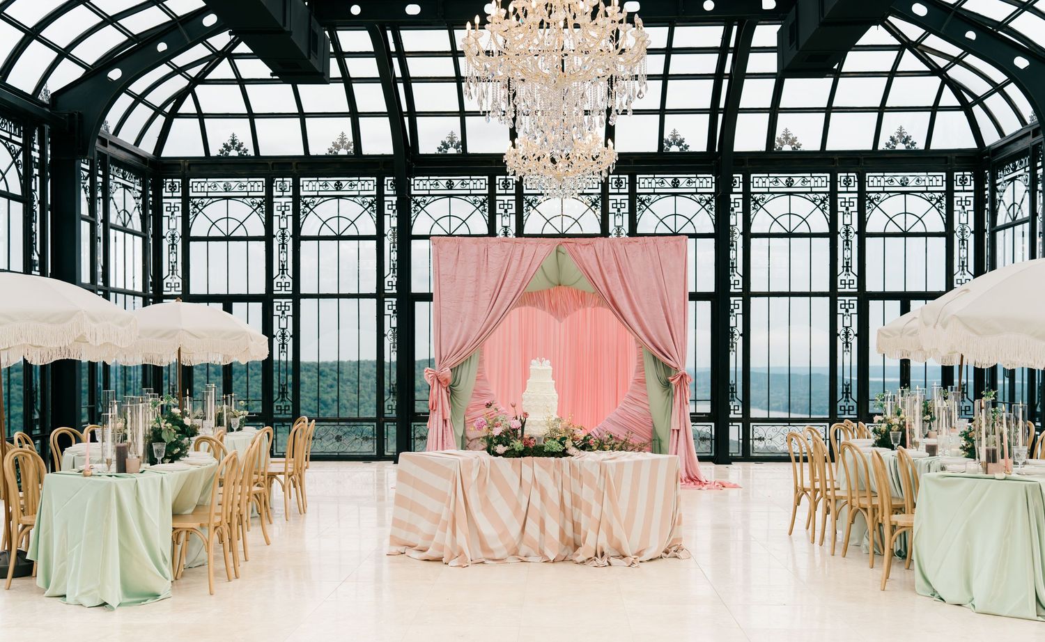 Elegant wedding reception in a glass conservatory with pink draping, chandelier, and mint green tablecloths.