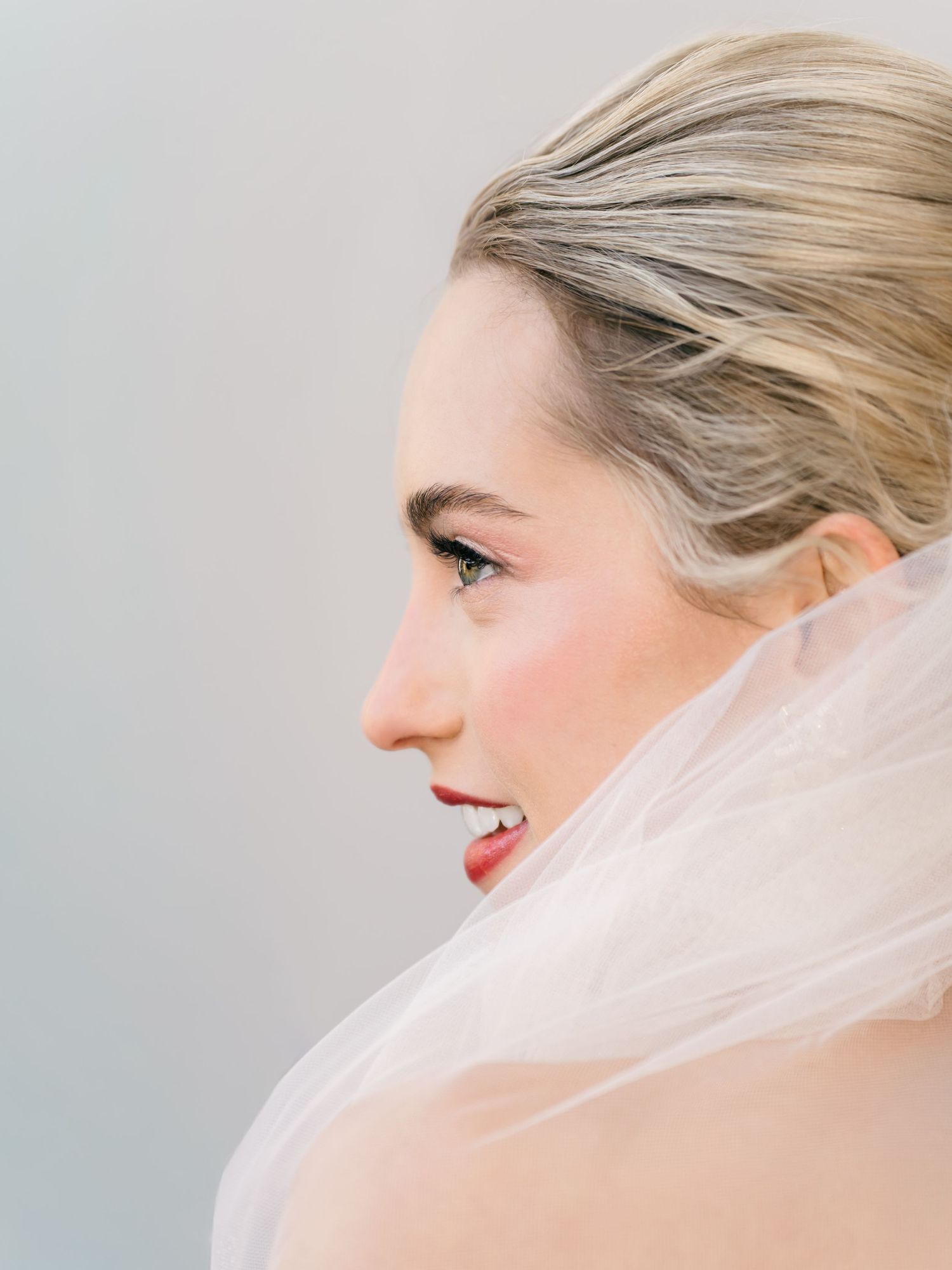 Side profile view of a bride wearing a delicate tulle veil with soft blonde hair styled up in an elegant updo.