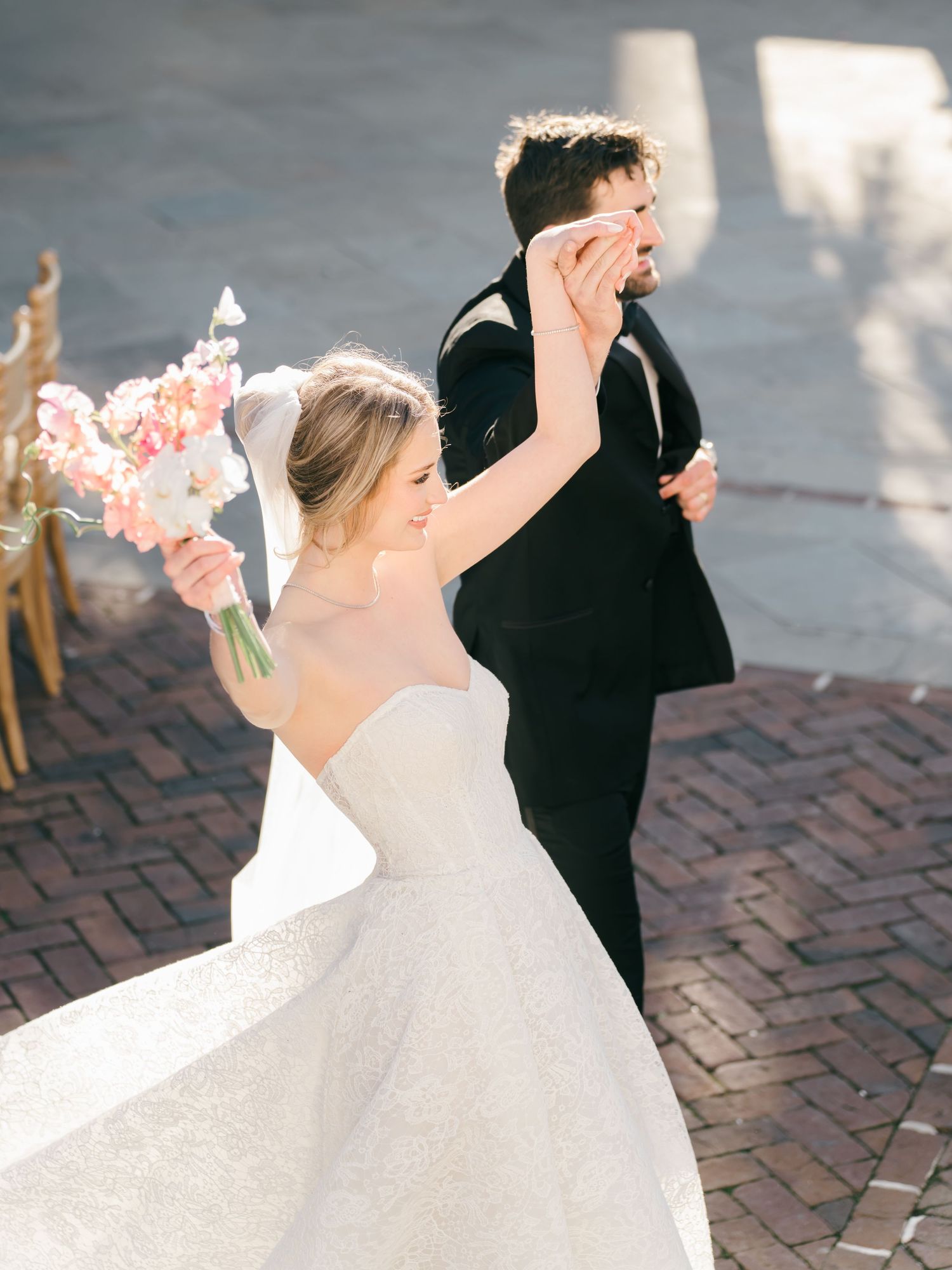 A couple in wedding attire dances together on a brick paved courtyard in a series of romantic poses.