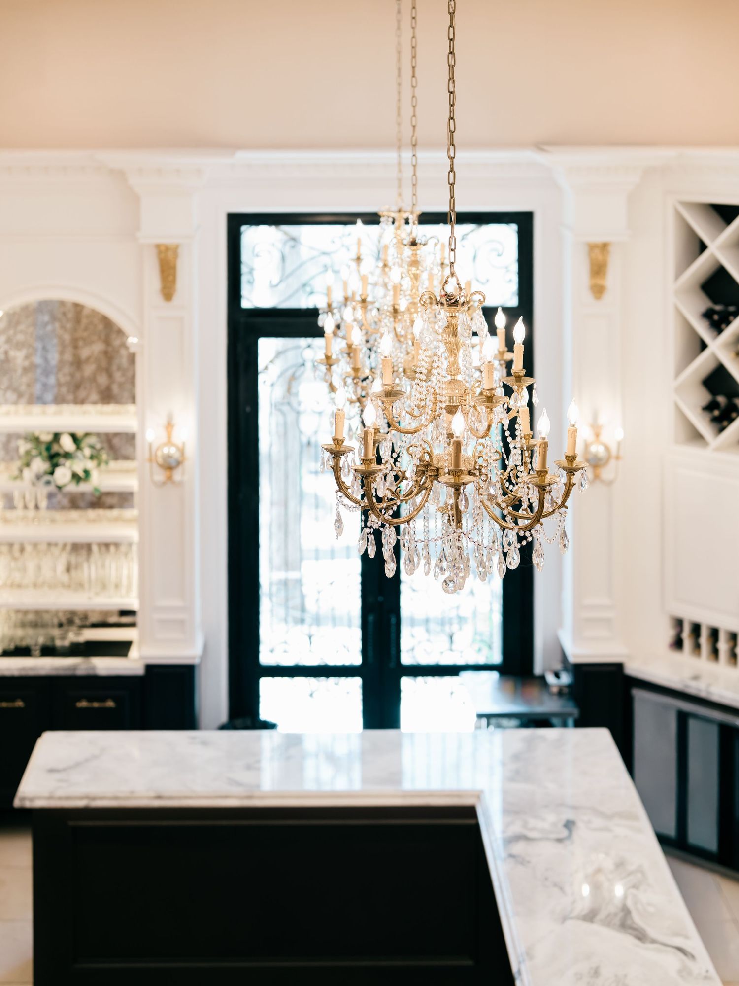 Elegant marble kitchen with crystal chandeliers, white cabinetry and black accents creating a luxurious modern space.