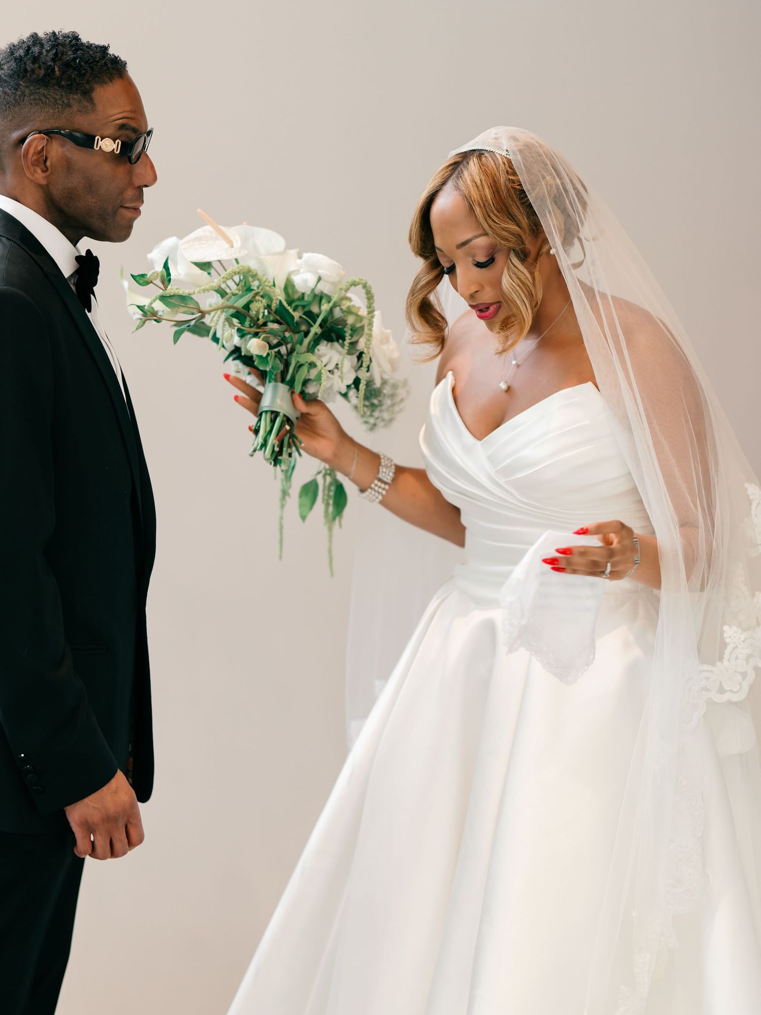 A wedding couple sharing a joyful moment as the bride in a white gown holds a simple white and green floral bouquet.