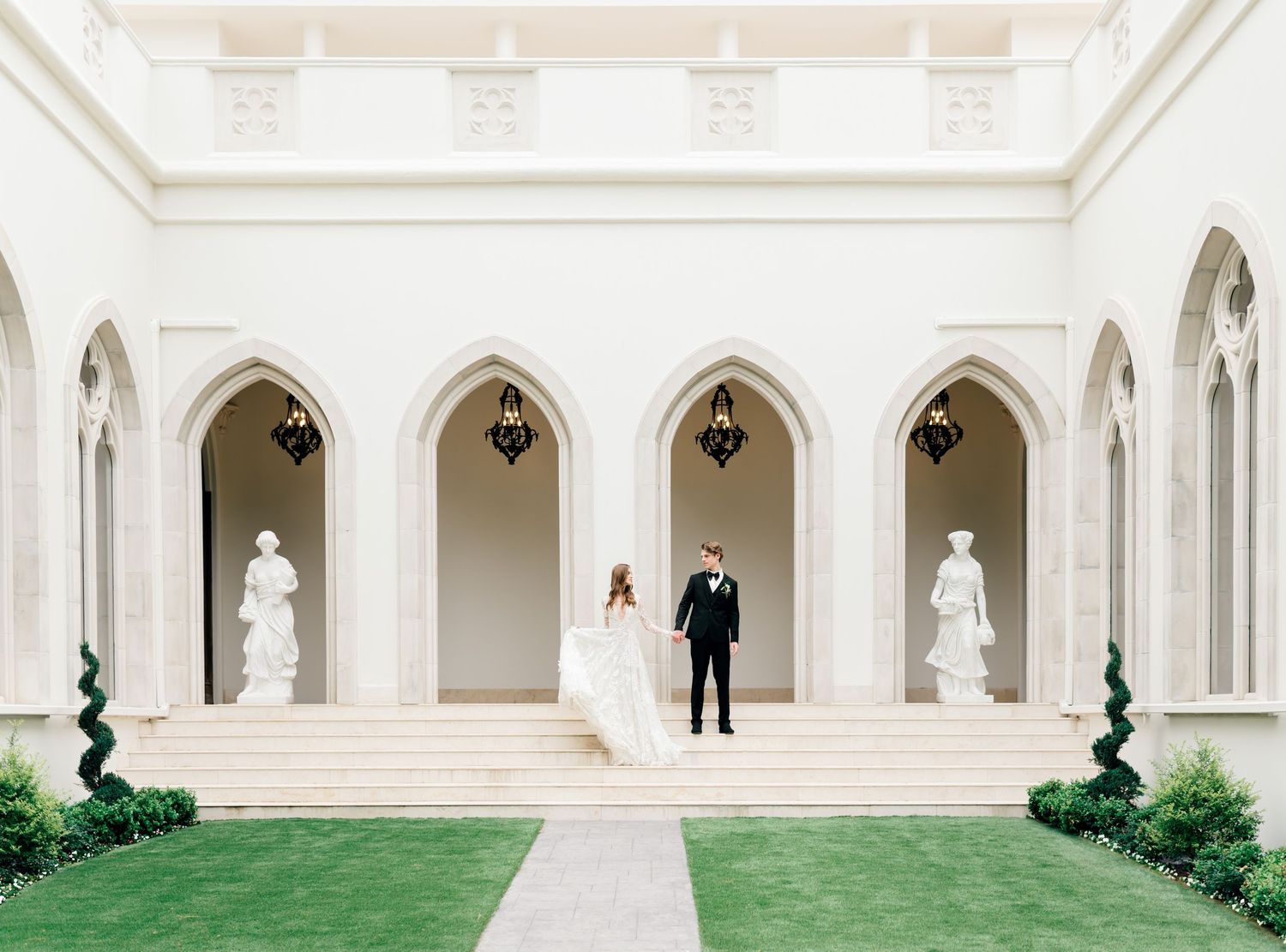 A panoramic view of an elegant white colonnade walkway with arched columns and green sculptures in a formal garden setting.